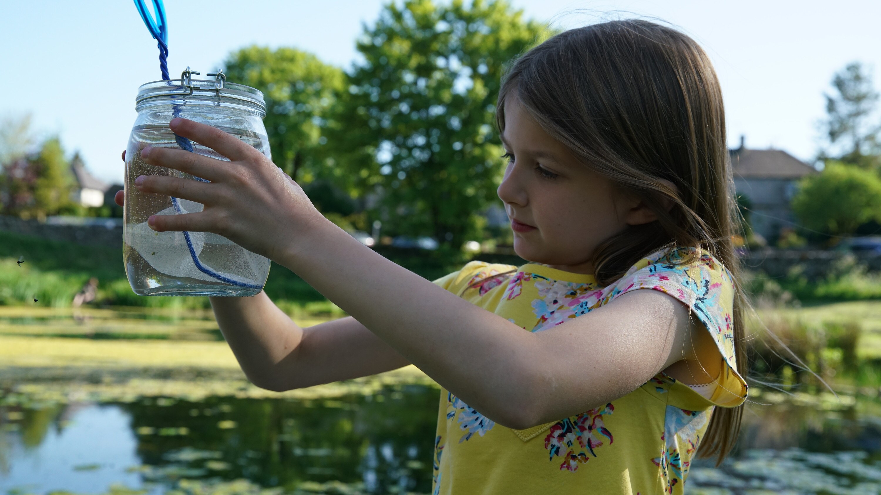 Young actor Menna holds a glass jar and plastic net near a pond in the "Once A Pond A Time" episode of "A Real Bug's Life." (National Geographic/Josh Kingsley Jones)