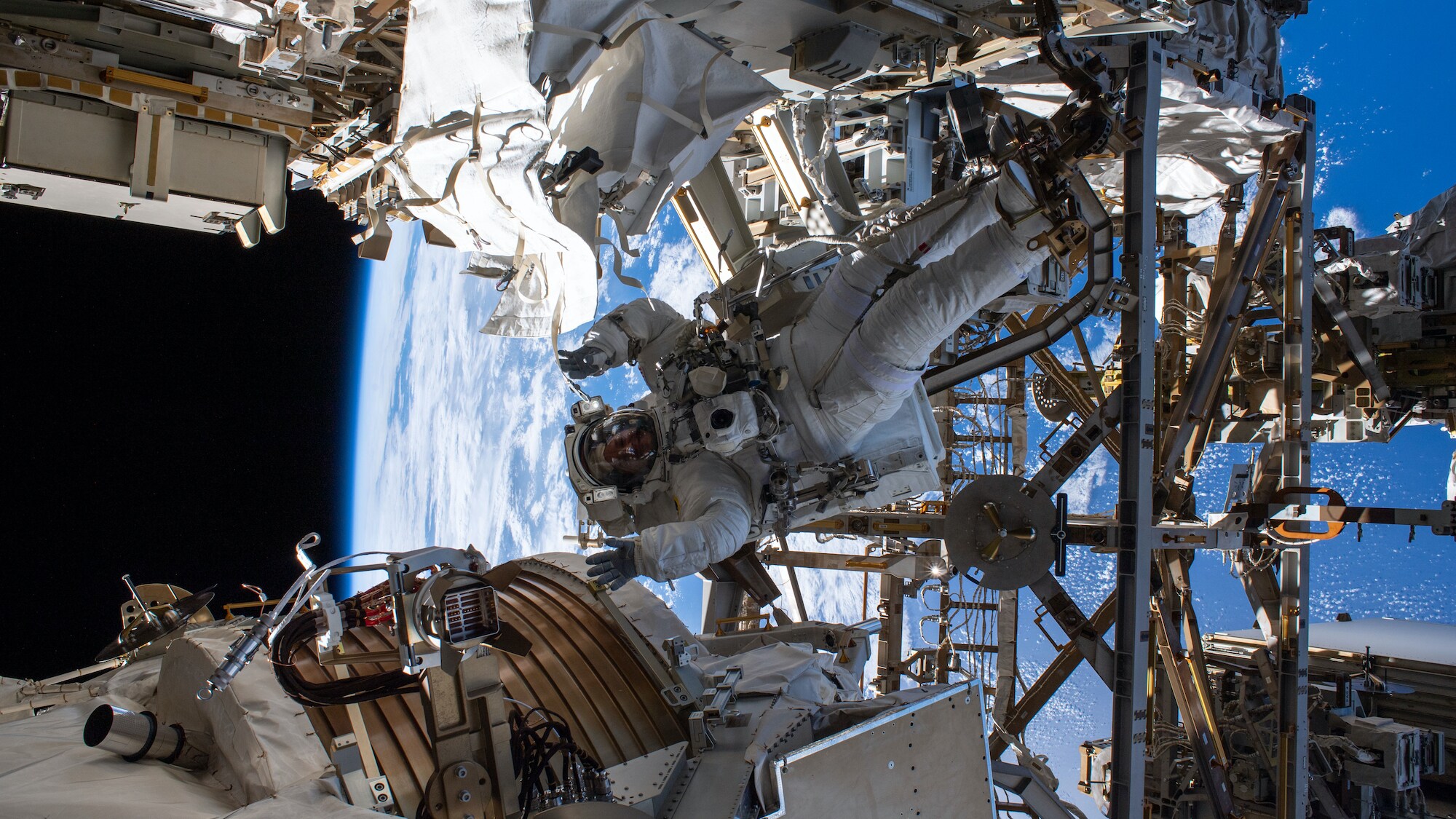 AMONG THE STARS - (Nov. 15, 2019) - NASA astronaut Andrew Morgan waves as he is photographed seemingly camouflaged among the Alpha Magnetic Spectrometer (lower left) and other International Space Station hardware during the first spacewalk to repair the cosmic particle detector. (NASA) ANDREW MORGAN