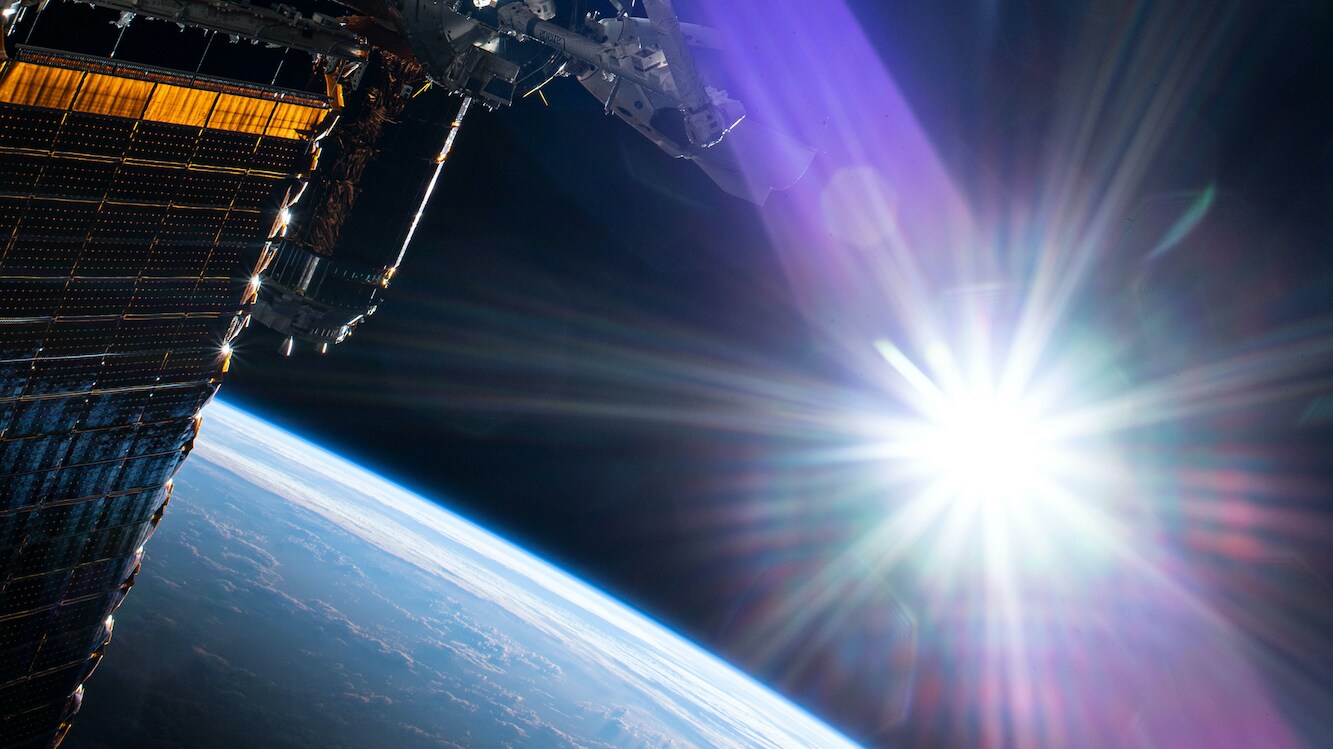 AMONG THE STARS - (July 21, 2020) - The sun beams just above the Earth's horizon as NASA astronaut and Expedition 63 Commander Chris Cassidy (center left) conducts his fourth spacewalk this year at the International Space Station. Cassidy has completed 10 spacewalks throughout his career for a total of 54 hours and 51 minutes spacewalking time. (NASA) CHRIS CASSIDY