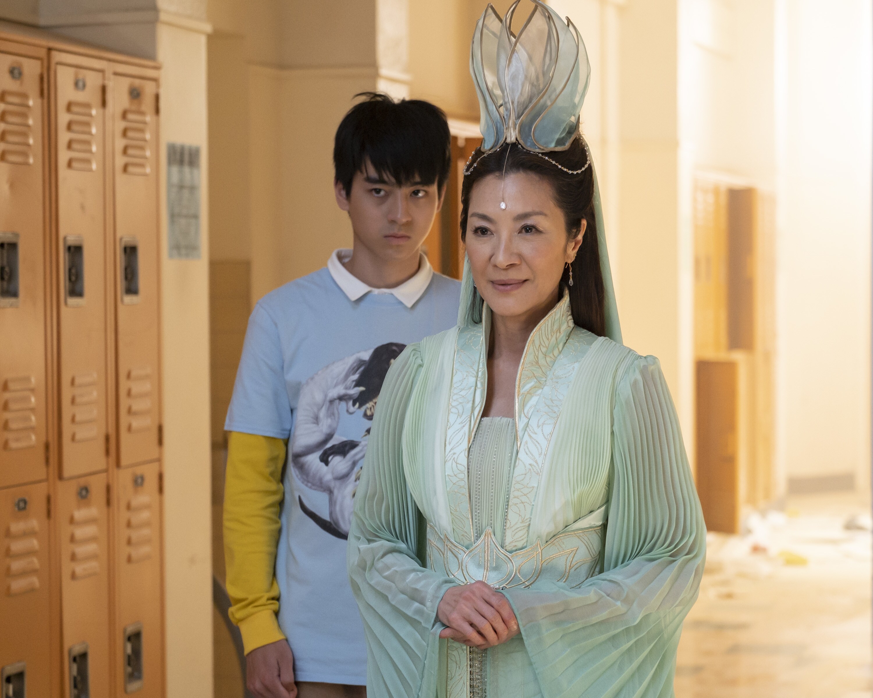 Guanyin (Michelle Yeoh), in a fantastical dress, stands in front of Wei-Chen (Jim Liu) in a high school hallway