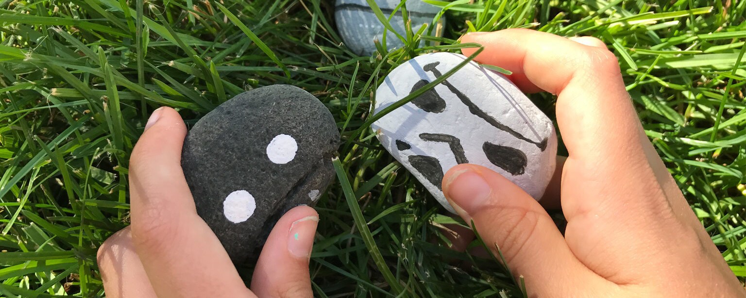 A child plays in the grass with stones decorated as K-2SO and a stormtrooper.