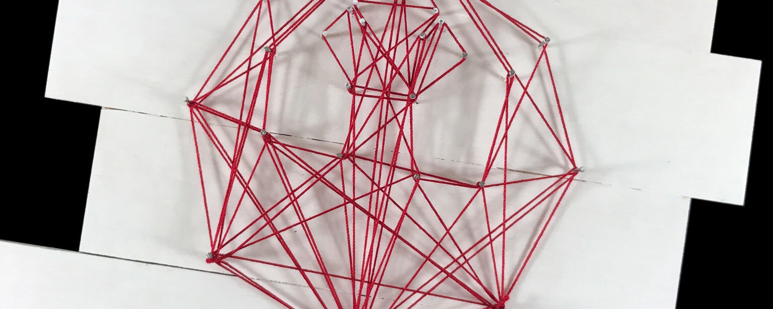 A string art craft in the shape of the Rebel insignia made with red string constructed on white wood.