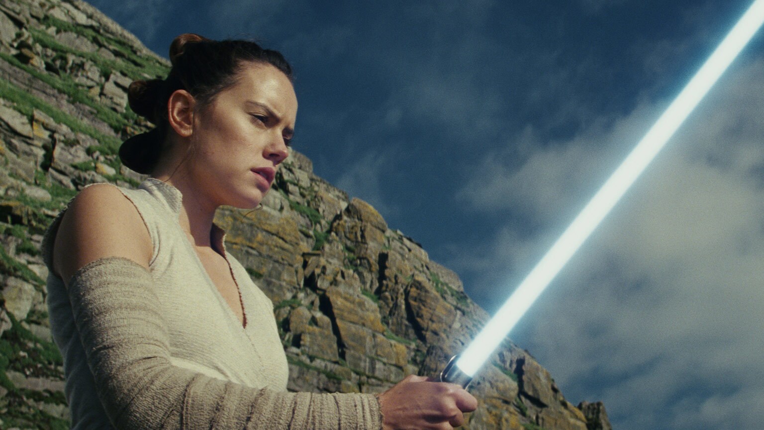 Rey holds a lightsaber in Star Wars: The Last Jedi.