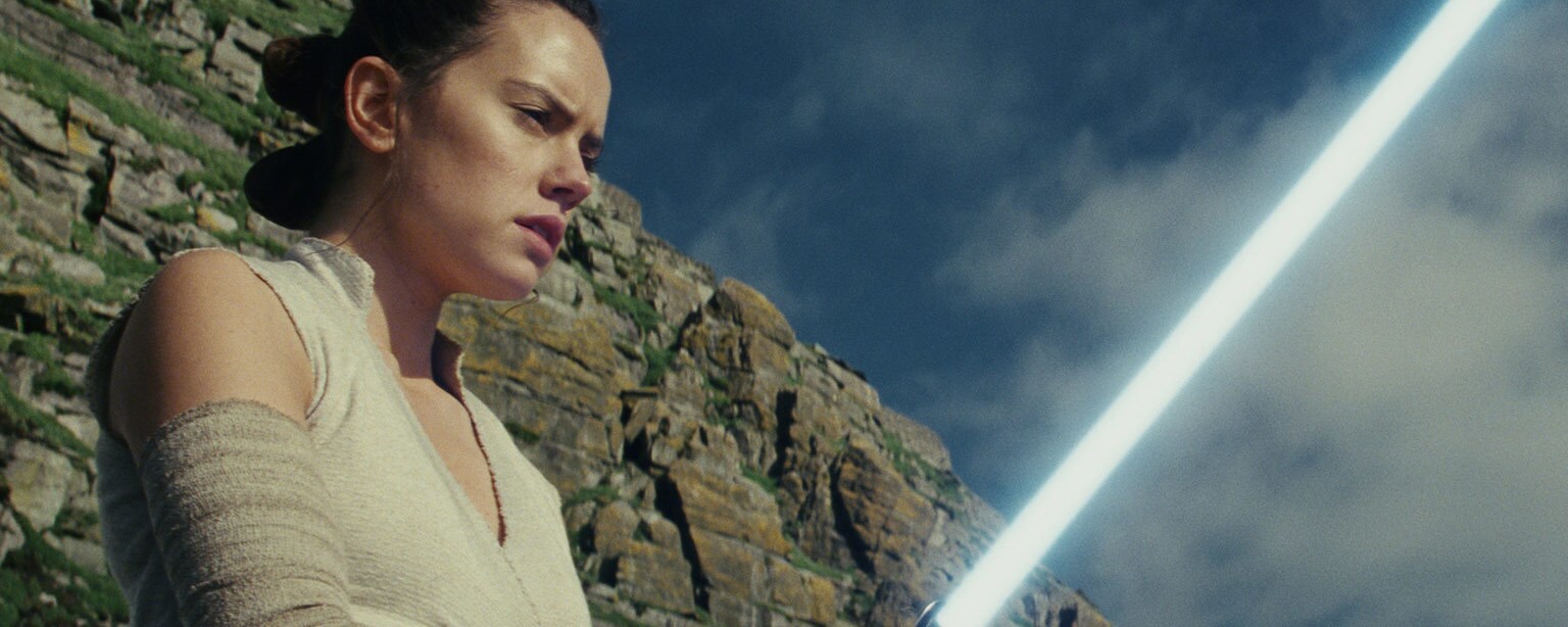 Rey holds a lightsaber in Star Wars: The Last Jedi.