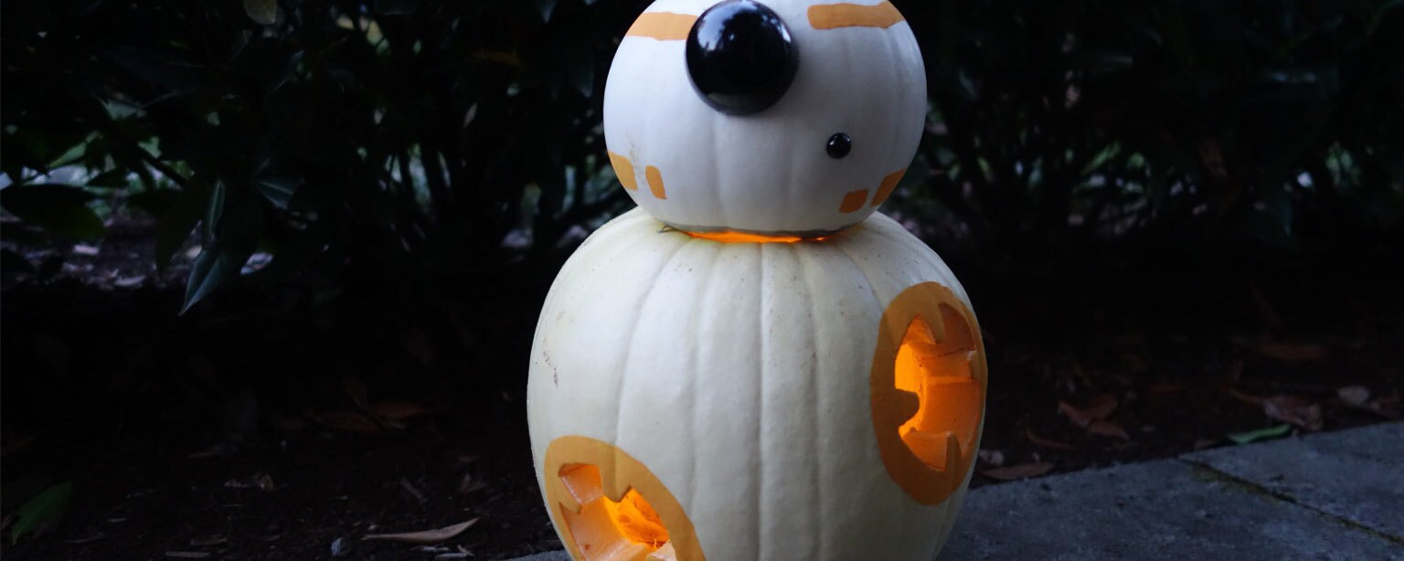 A BB-8 jack-o-lantern made from two white pumpkins stacked on top of each other, carved and decorated with orange and silver paint.