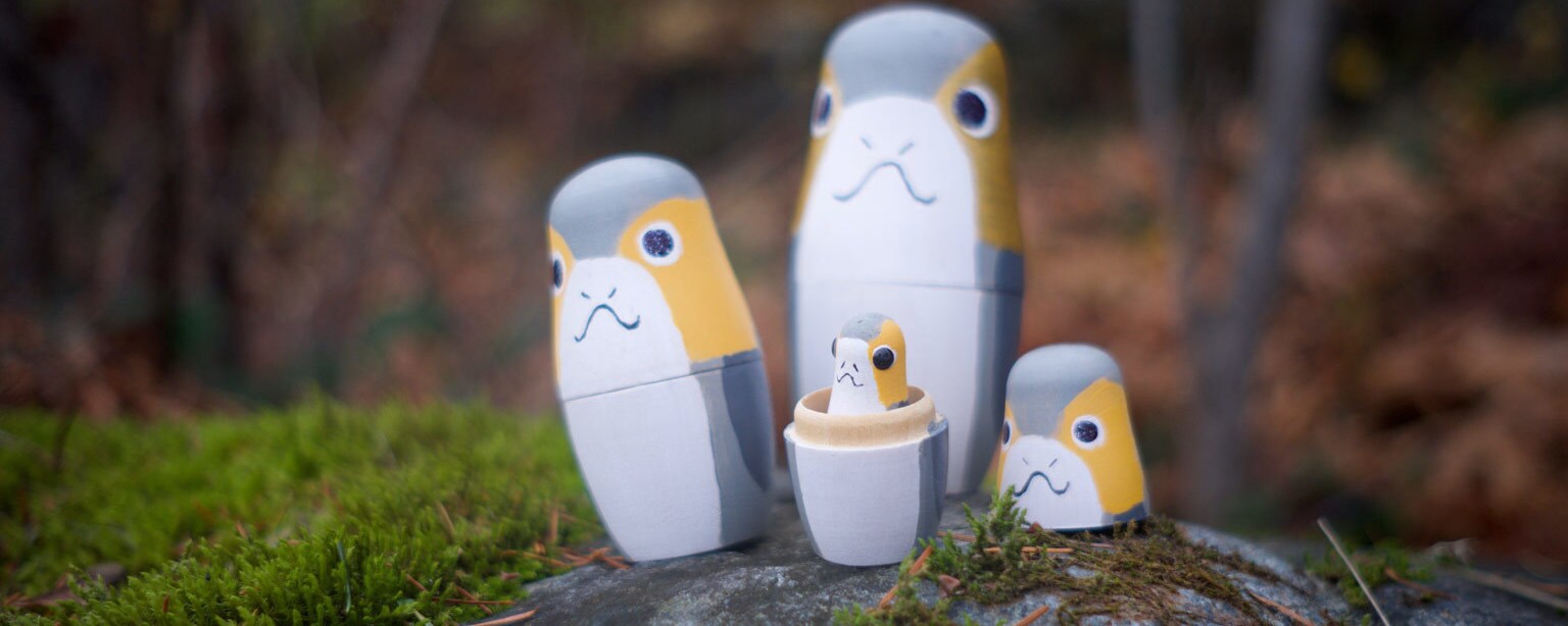 A group of nesting dolls painted to look like Porgs sitting on a moss covered rock.