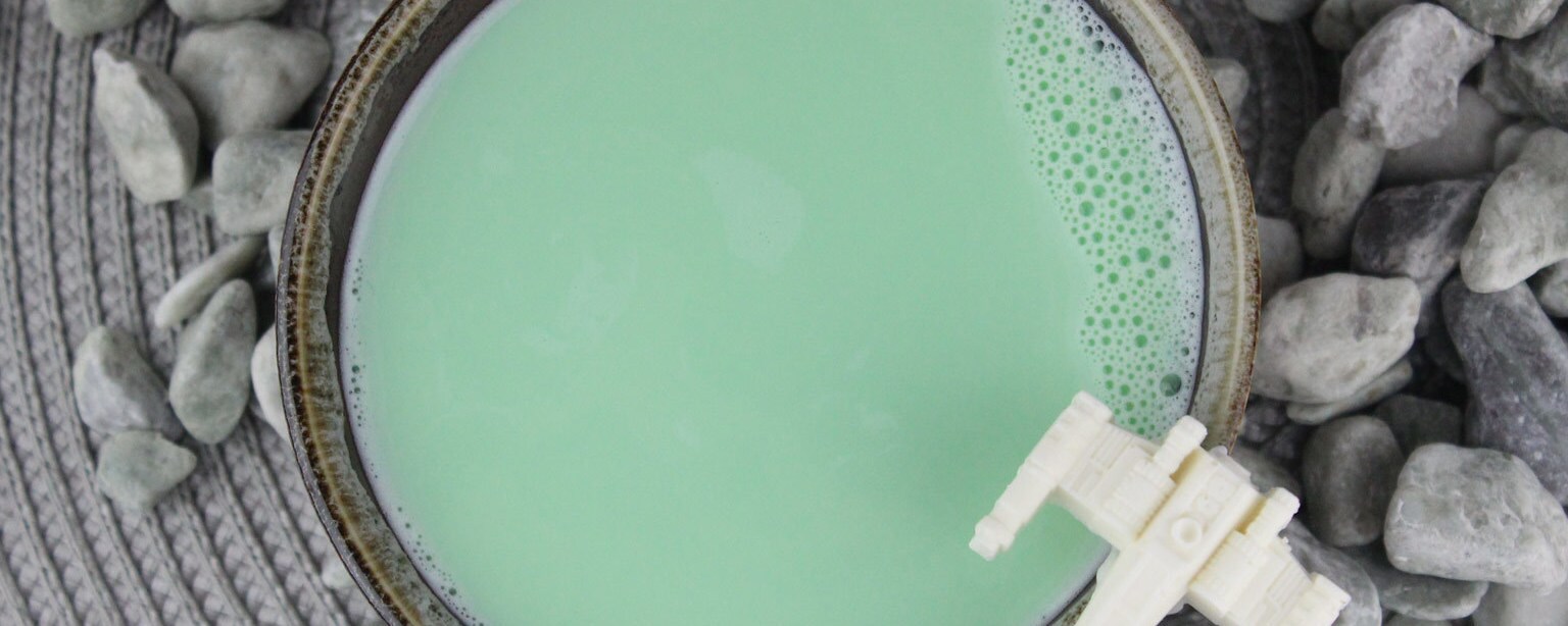 A mug of green milk with a white X-wing on the rim, as viewed from above.