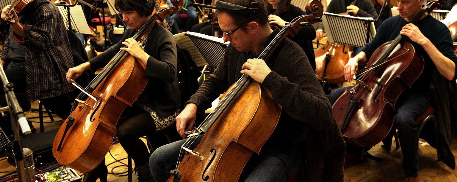 The bass section of an orchestra wears headphones while playing during a recording session.