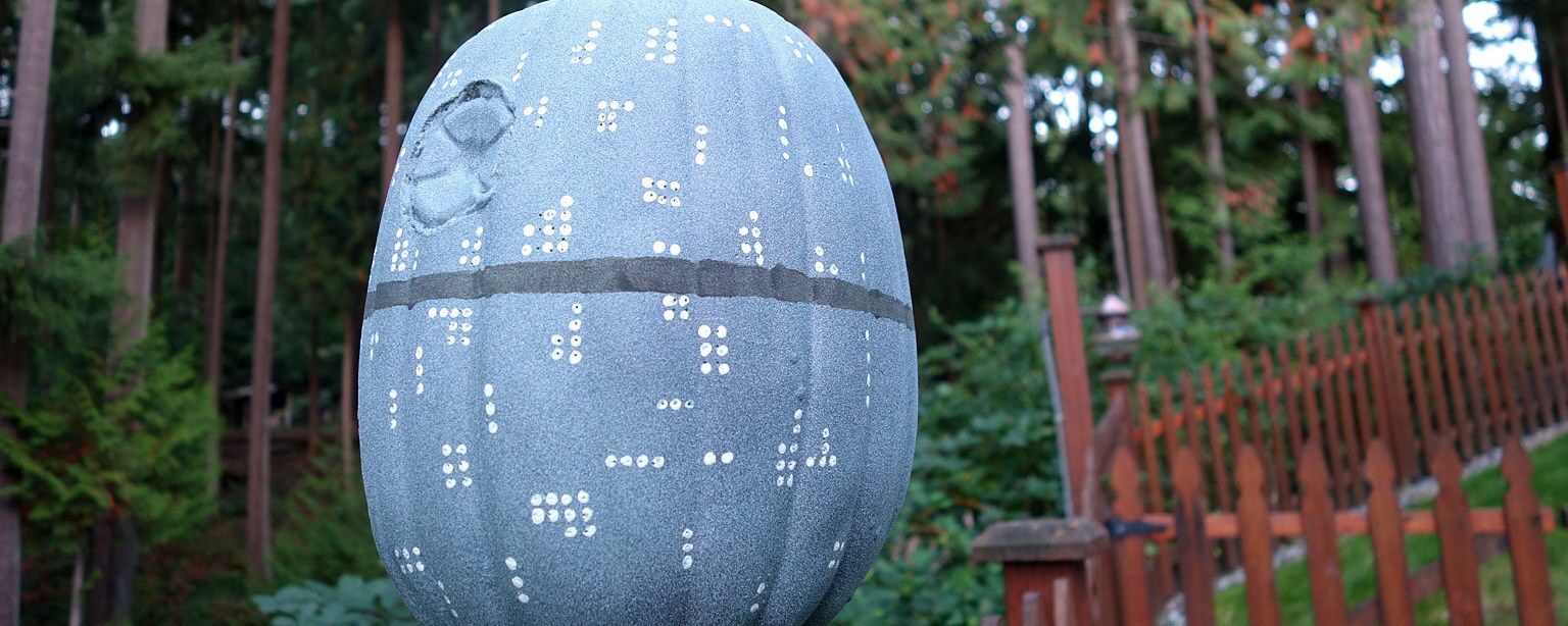 A pumpkin made to look like the Death Star sits on top of a fence post.