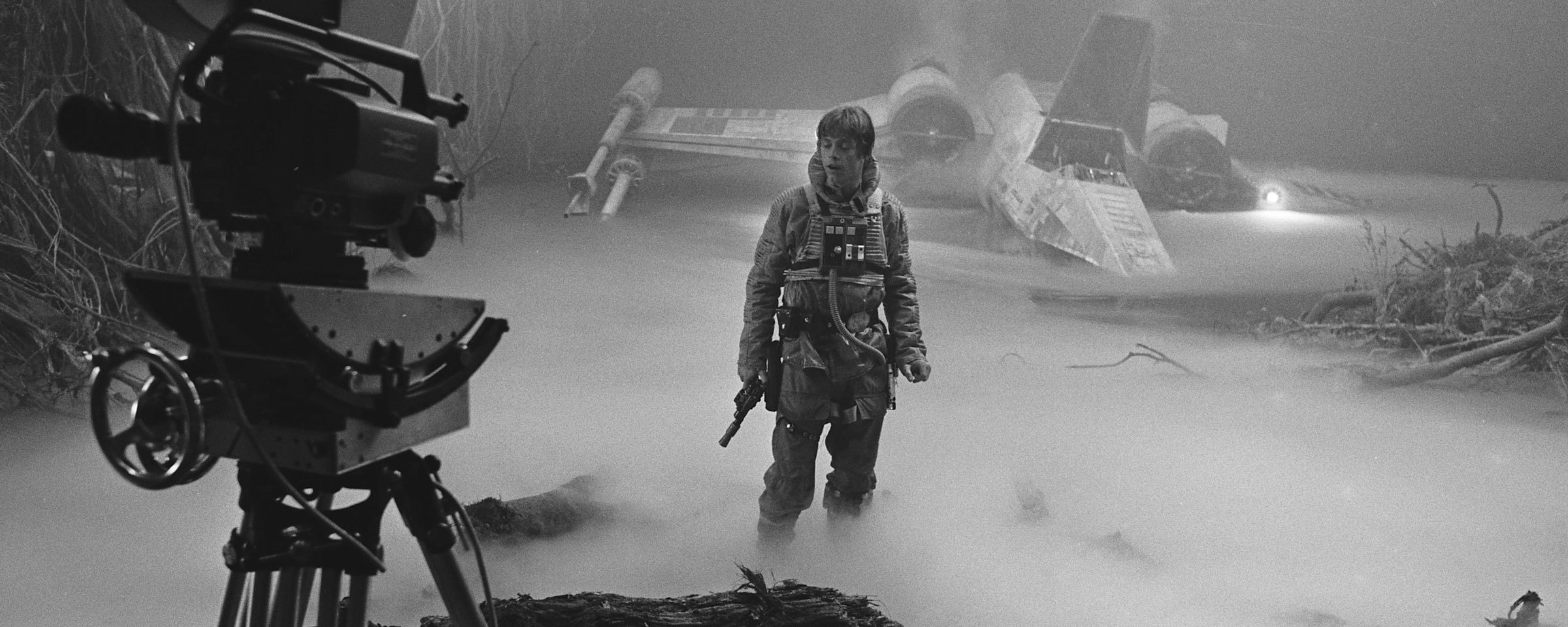 A behind-the-scenes photo from The Empire Strikes Back shows a movie camera, in the foreground, capturing a scene of Luke Skywalker on Dagobah with with his starfighter in the background.