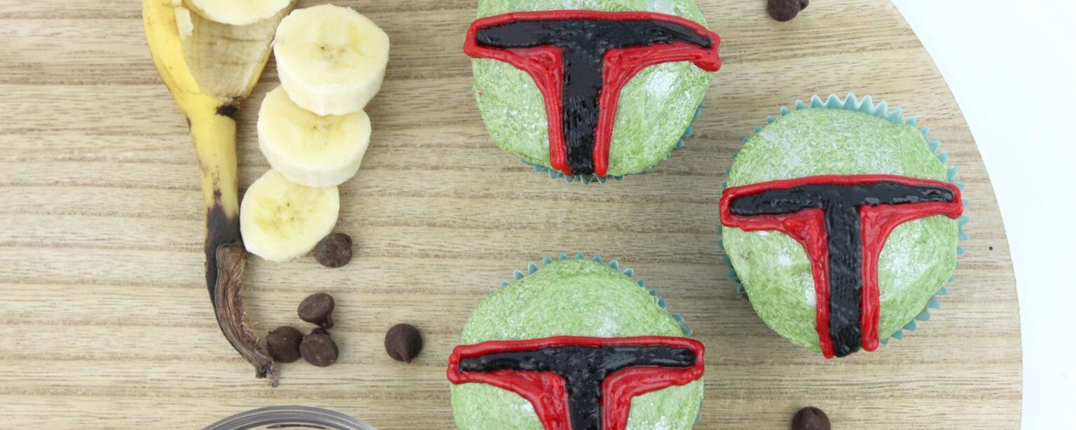 Three Boba Fett muffins sit on a table next to a sliced banana and chocolate chips.
