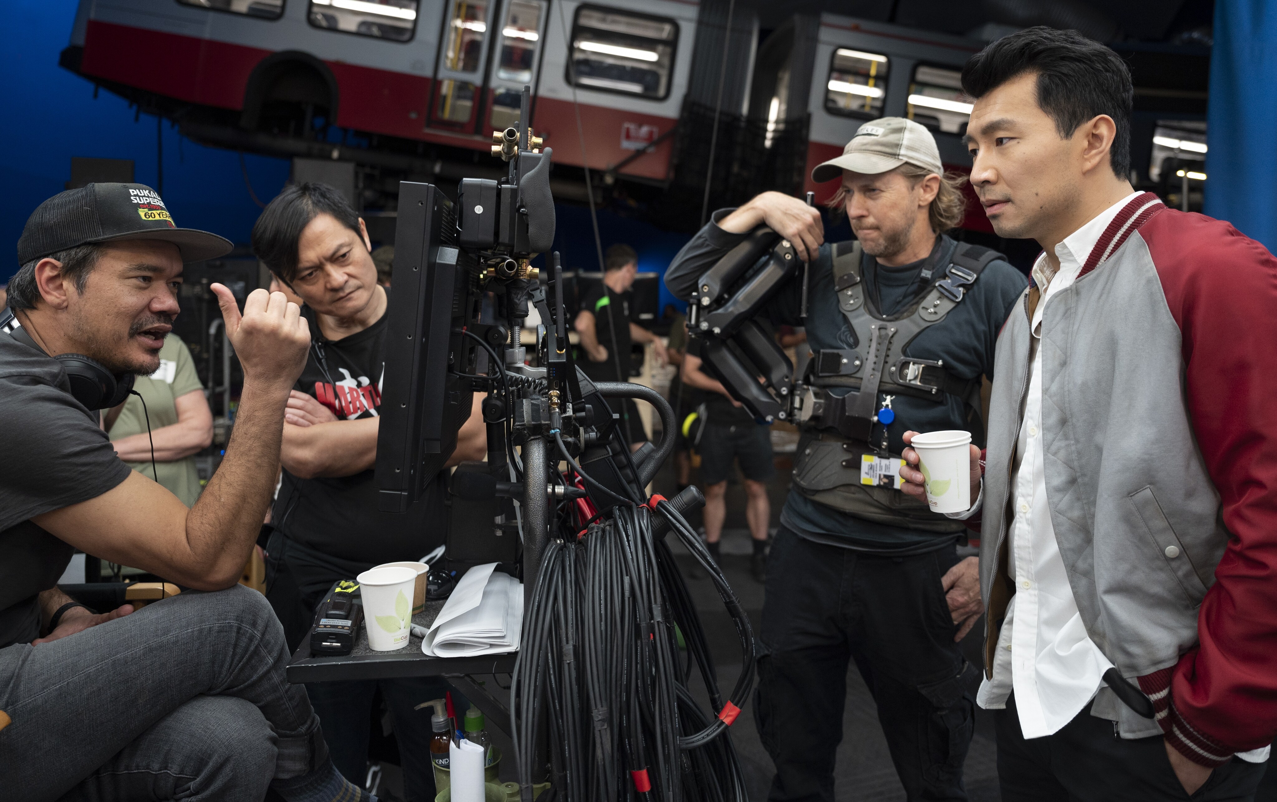 Director Destin Daniel Cretton looks at the monitor and chats with his team, including actor Simu Liu, on set.