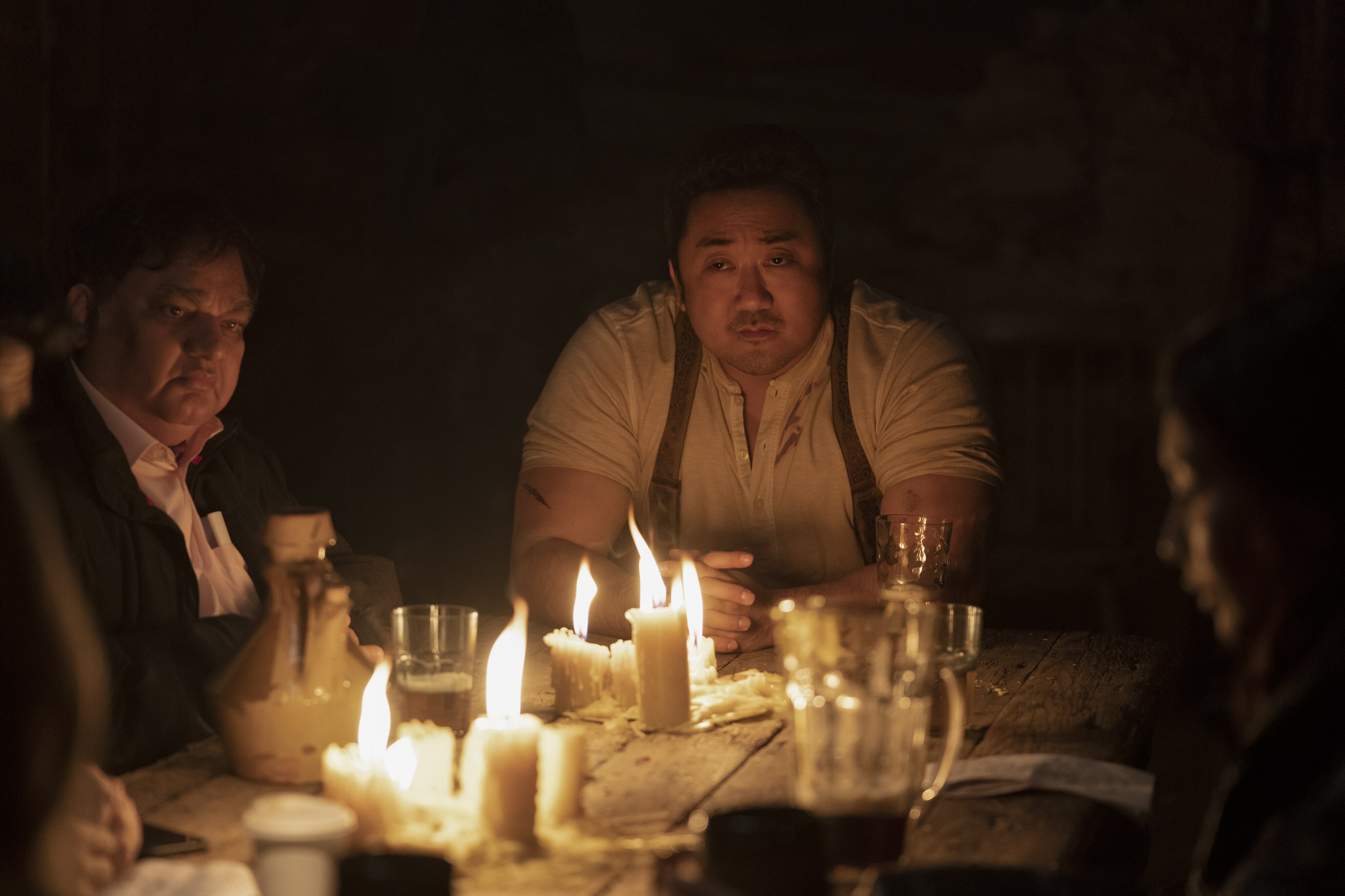 The Eternals sit around a dinner table lit by candlelight. Don Lee as Gilgamesh is visible at the head of the table, illuminated by candlelight. 