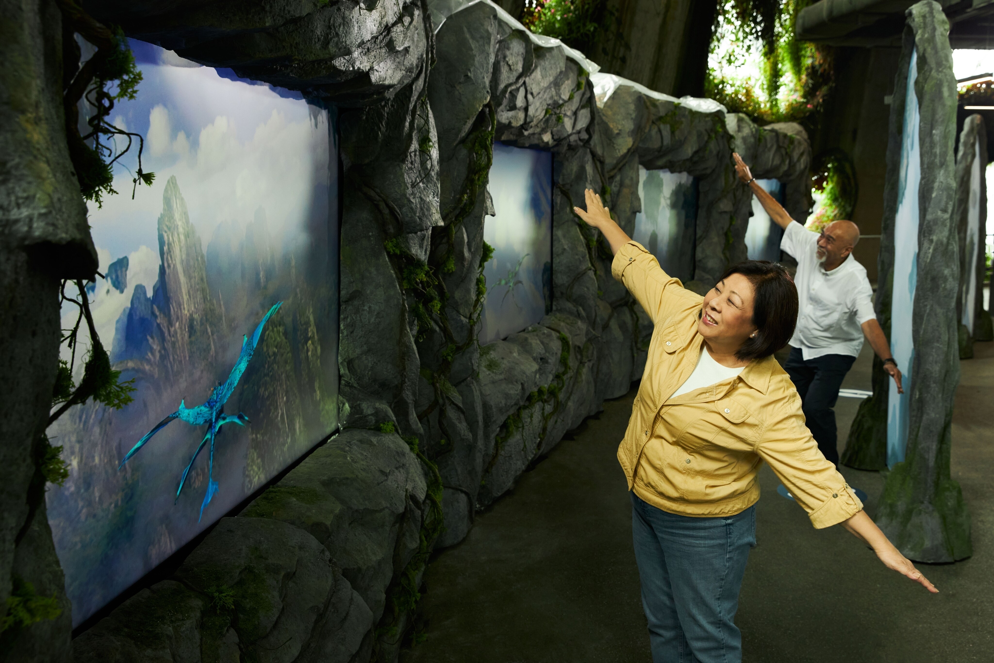 Two people mimicking flying like a banshee while watching teh banshees fly on a television screen.