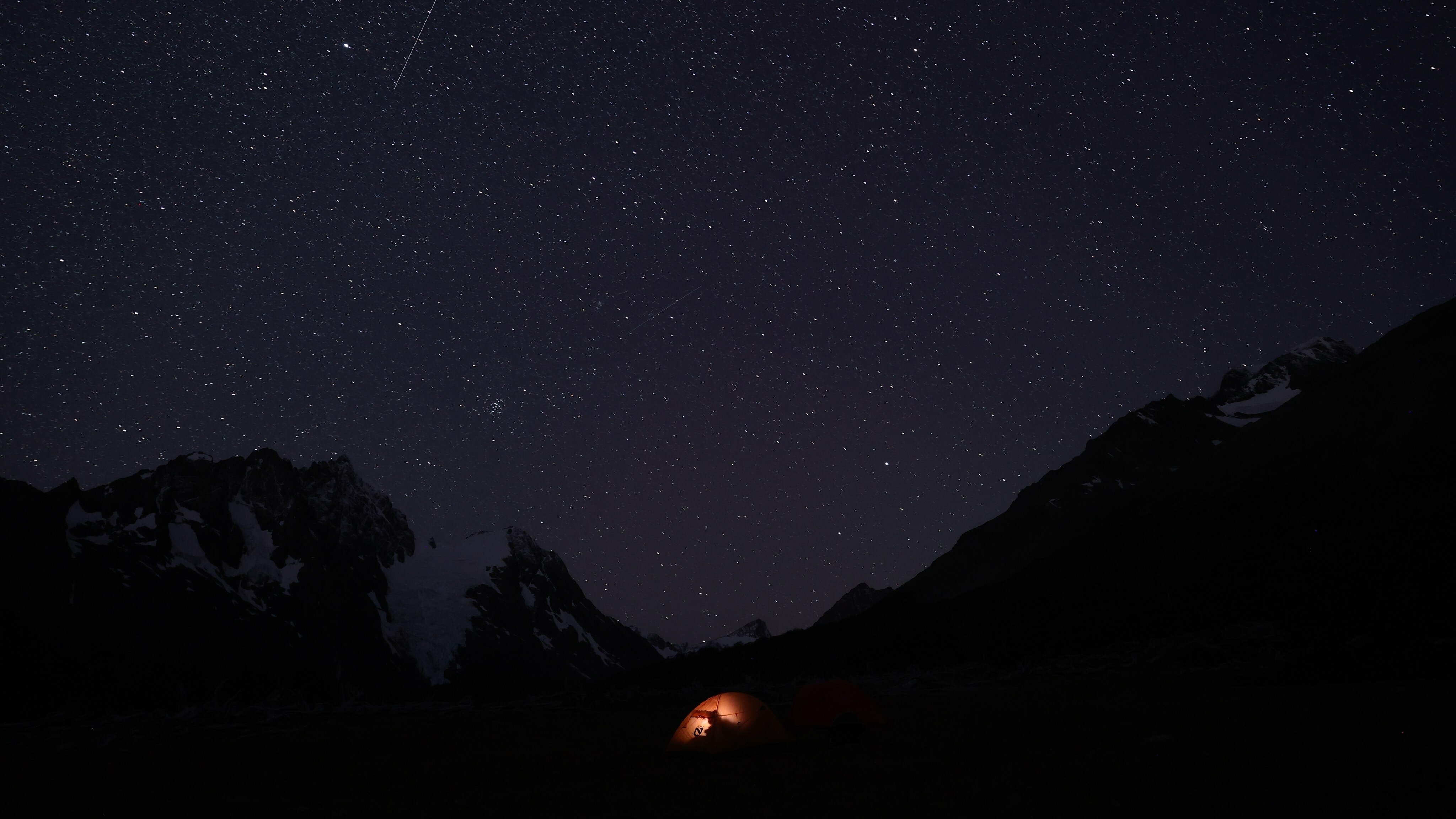 A starry night sky shown above small tent illuminated by an occupant. (Jimmy Chin)