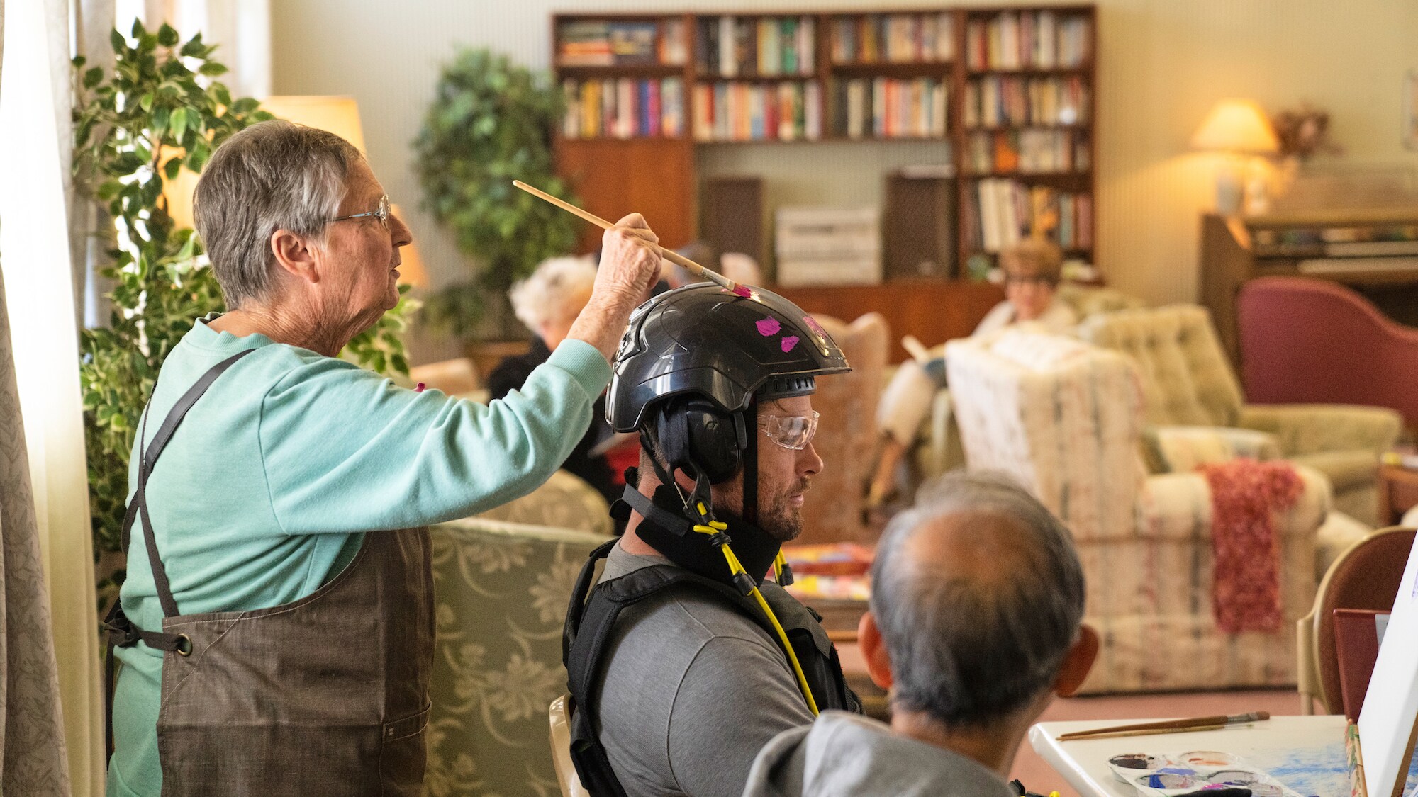 Chris Hemsworth takes part in an art class with other residents. One resident paints a rally stripe on Chris' helmet. (National Geographic for Disney+/Craig Parry)