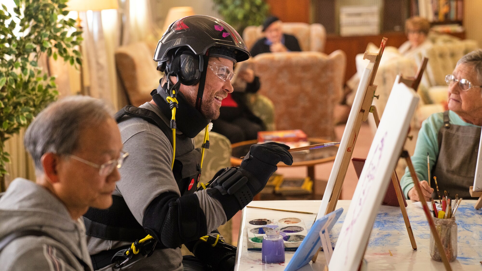 During the art class, Chris Hemsworth engages with other residents and learns from their experience of learning. Chris and others laugh at his painting. (National Geographic for Disney+/Craig Parry)