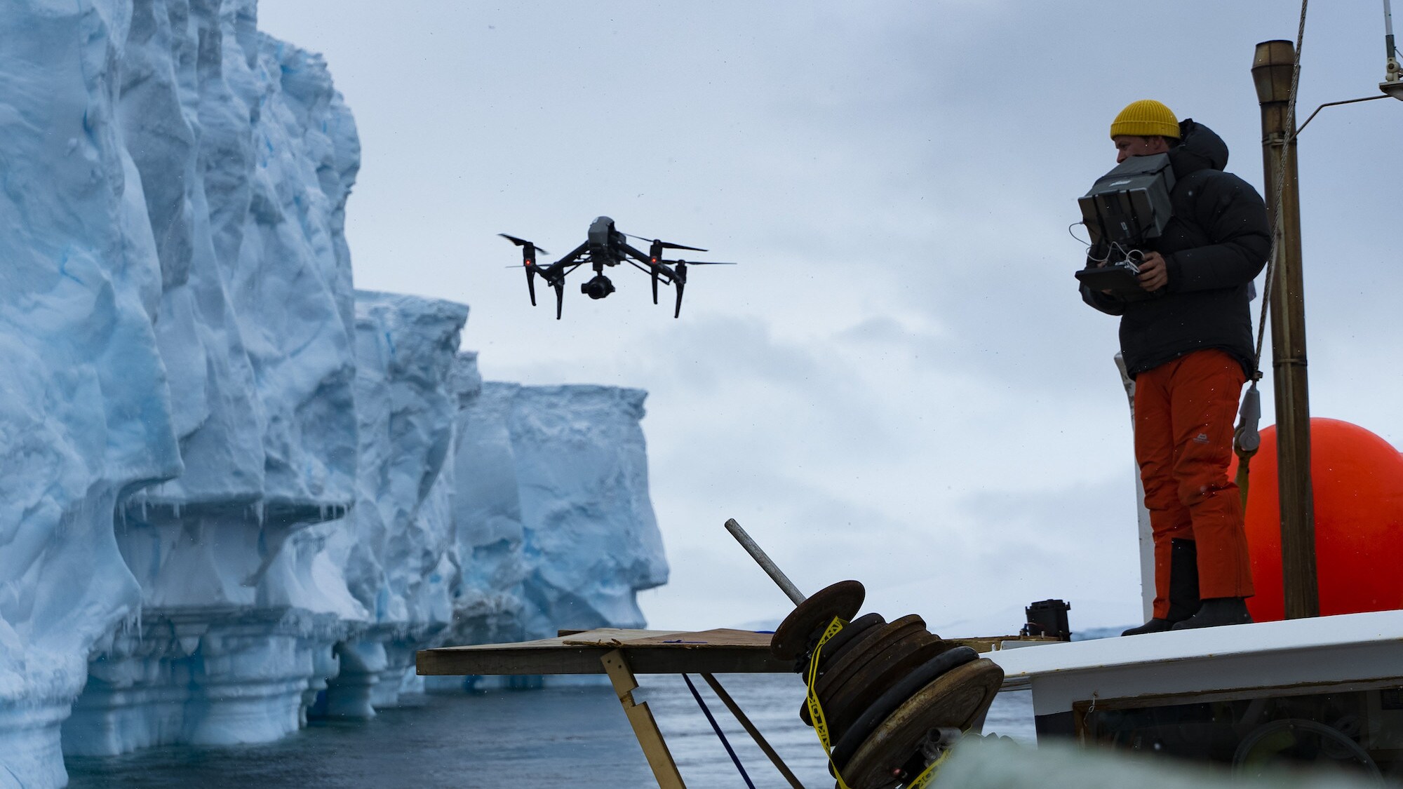 Bertie Gregory standing on a platform, flying a drone alongside an ice flow.  (credit: National Geographic for Disney+/Anna Dimitriadis)