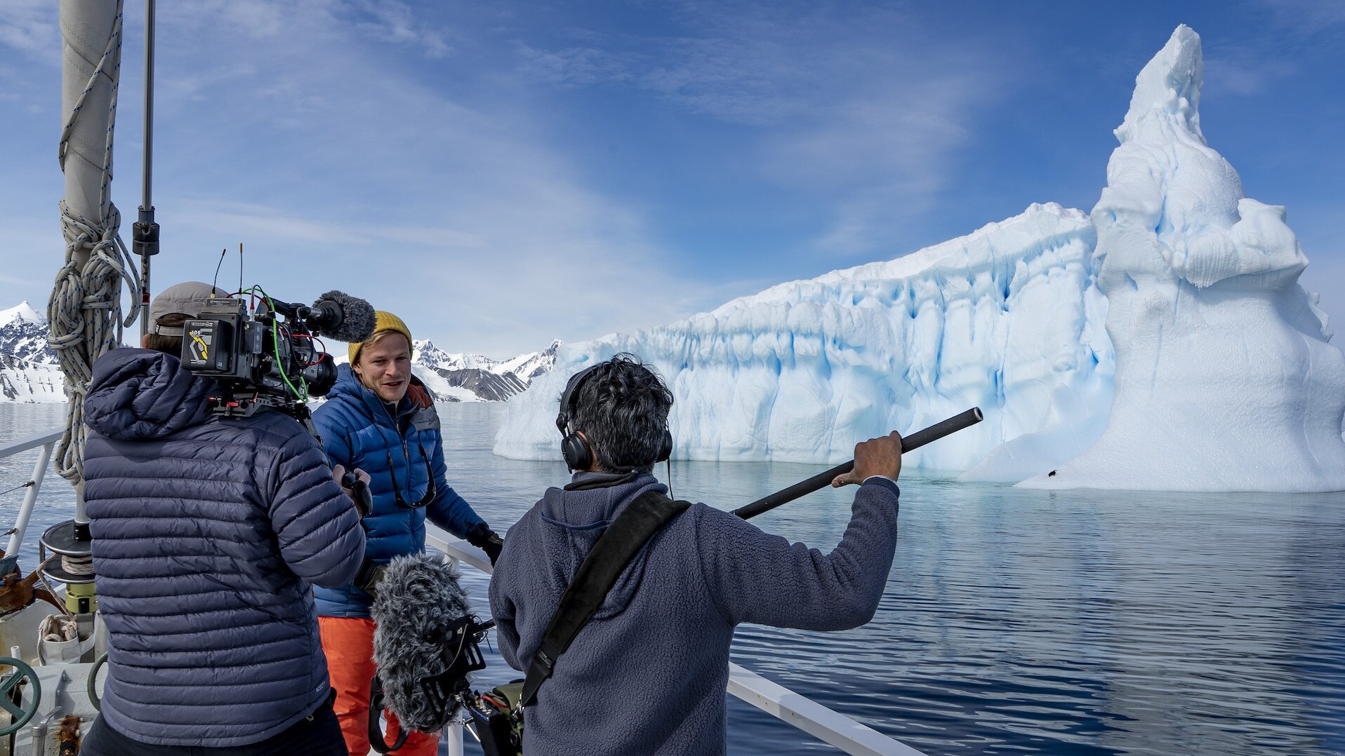 Bertie Gregory with camera operator and sound recordist, recording a piece to camera in front of a large iceberg. (credit: National Geographic for Disney+/Anna Dimitriadis)