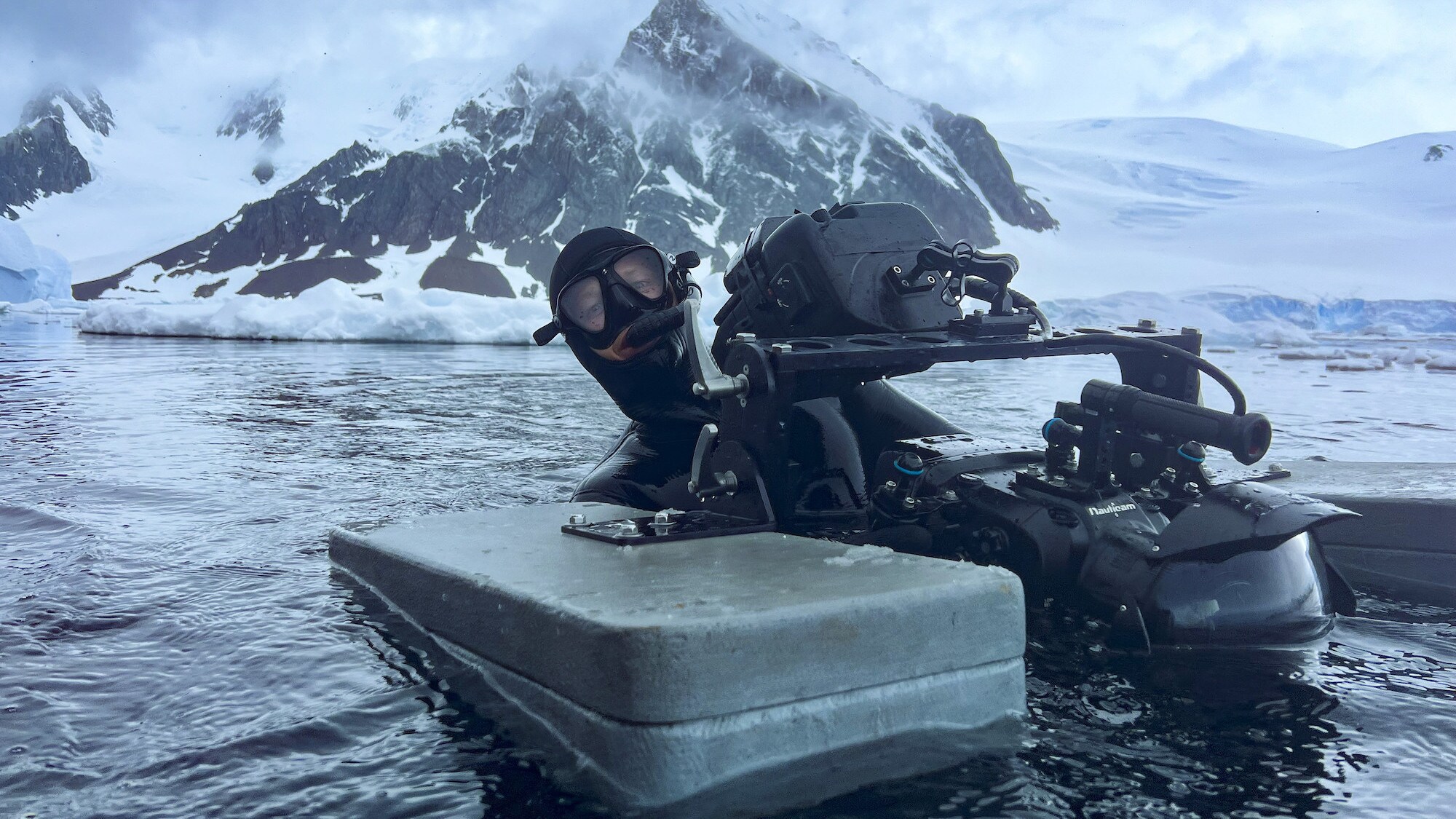 Masked Camera operator on the surface of the water holding a floated camera. (credit: National Geographic for Disney+/Calumn Stronach)