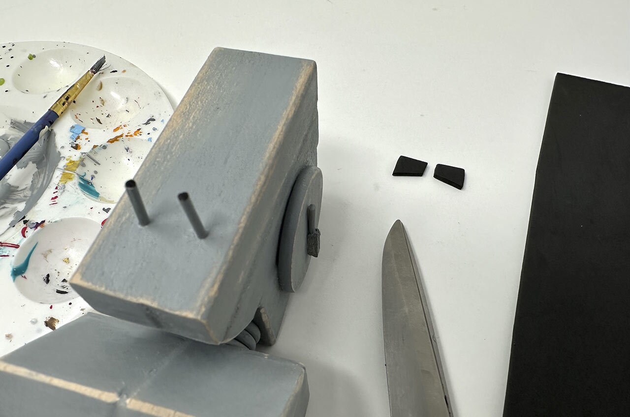 Step 27: Cut two small rectangular shapes from black craft foam, about 1 cm in length each, to make the “eyes” of the AT-ST. Glue them in place near the top of the face, then drybrush gray paint on the edges to add weathering.