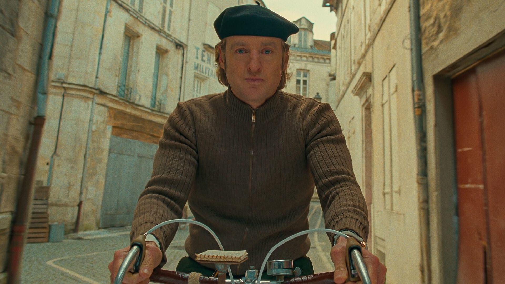 Actor Owen Wilson rides a bike in the film The French Dispatch
