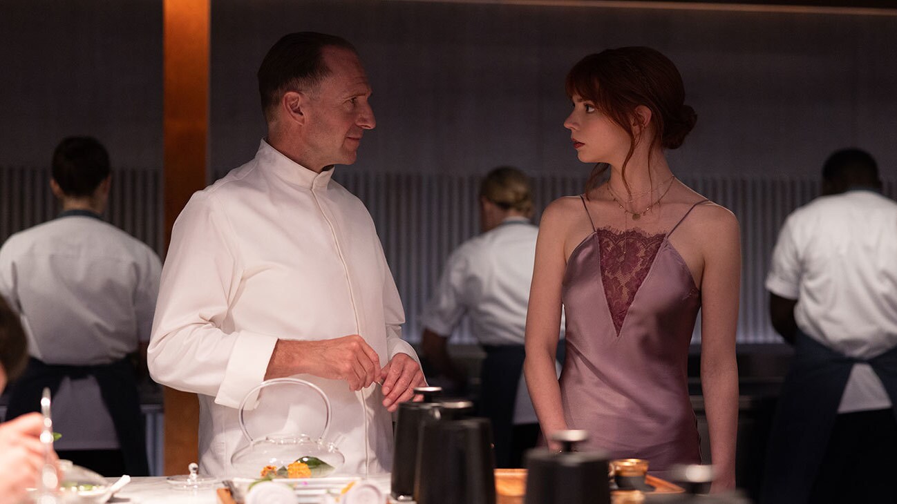 Chef, Ralph Fiennes looks towards another guests, speaking inside the restaurant with other workers in the background.