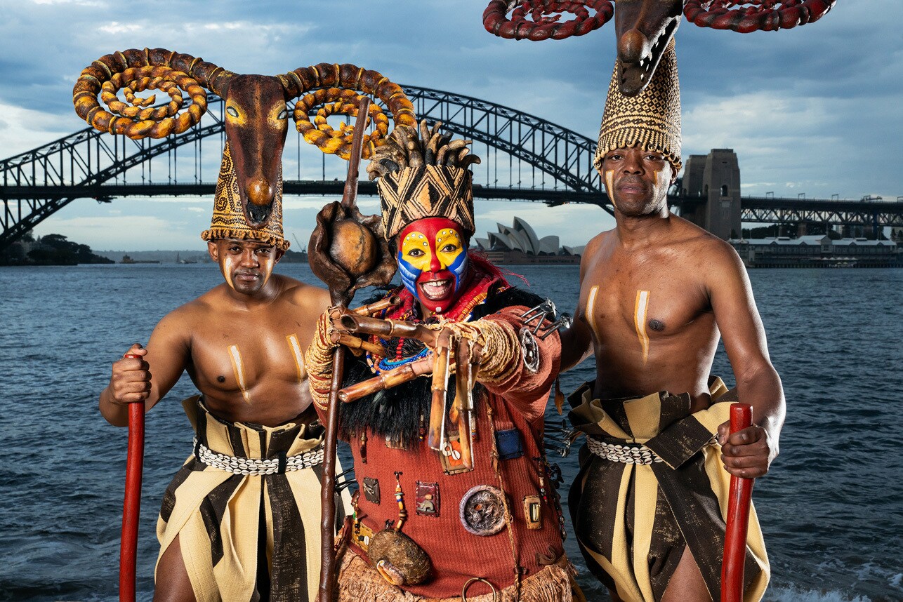 An image of the cast of The Lion King the musical standing in front of the Sydney Harbour Bridge