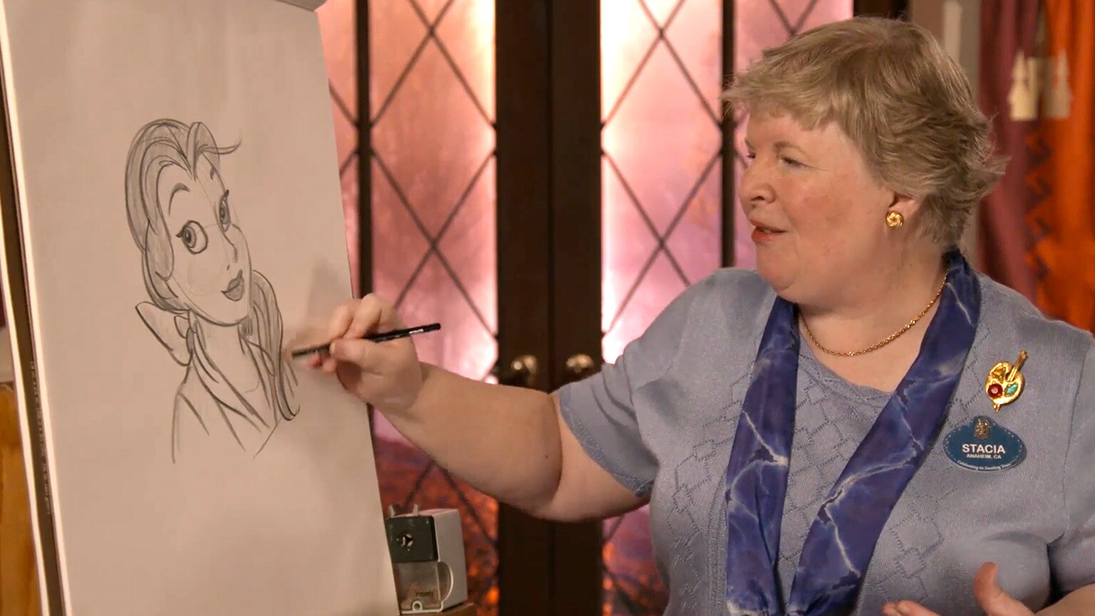 Disney artist and historian Stacia Martin stands in front of an easel and draws Belle from Beauty and the Beast