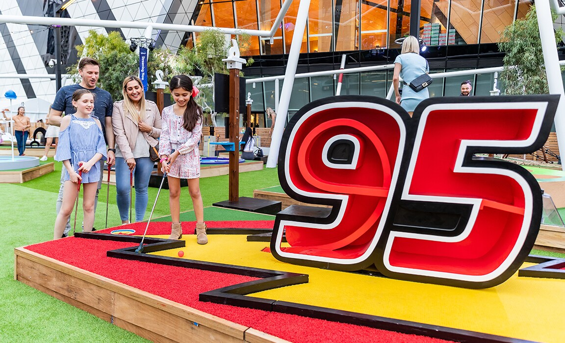 A young girl playing Pixar Putt in front of the Cars-themed number 95 hole