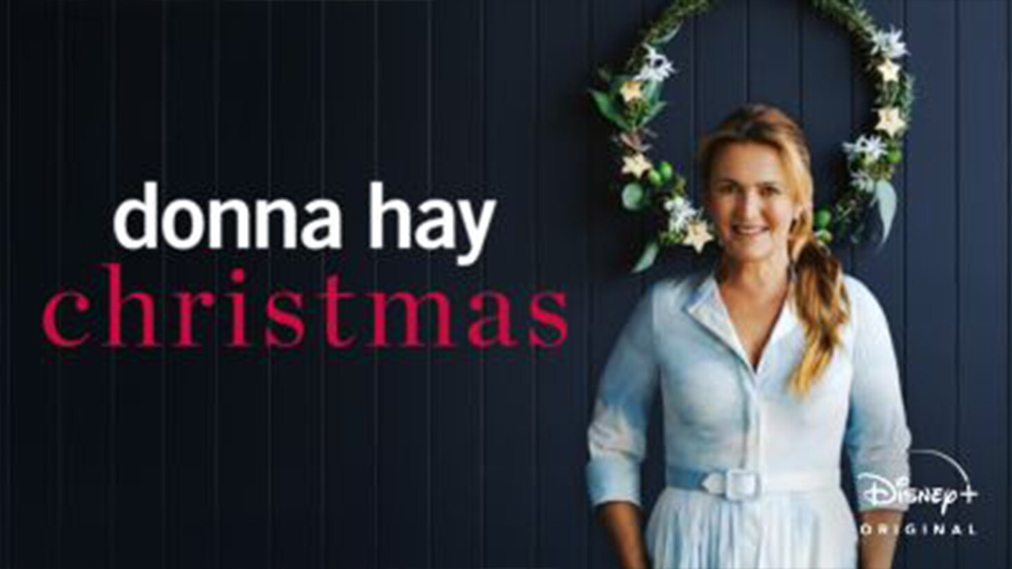 An image of Donna Hay standing in front of a christmas wreath, against a dark blue wall.