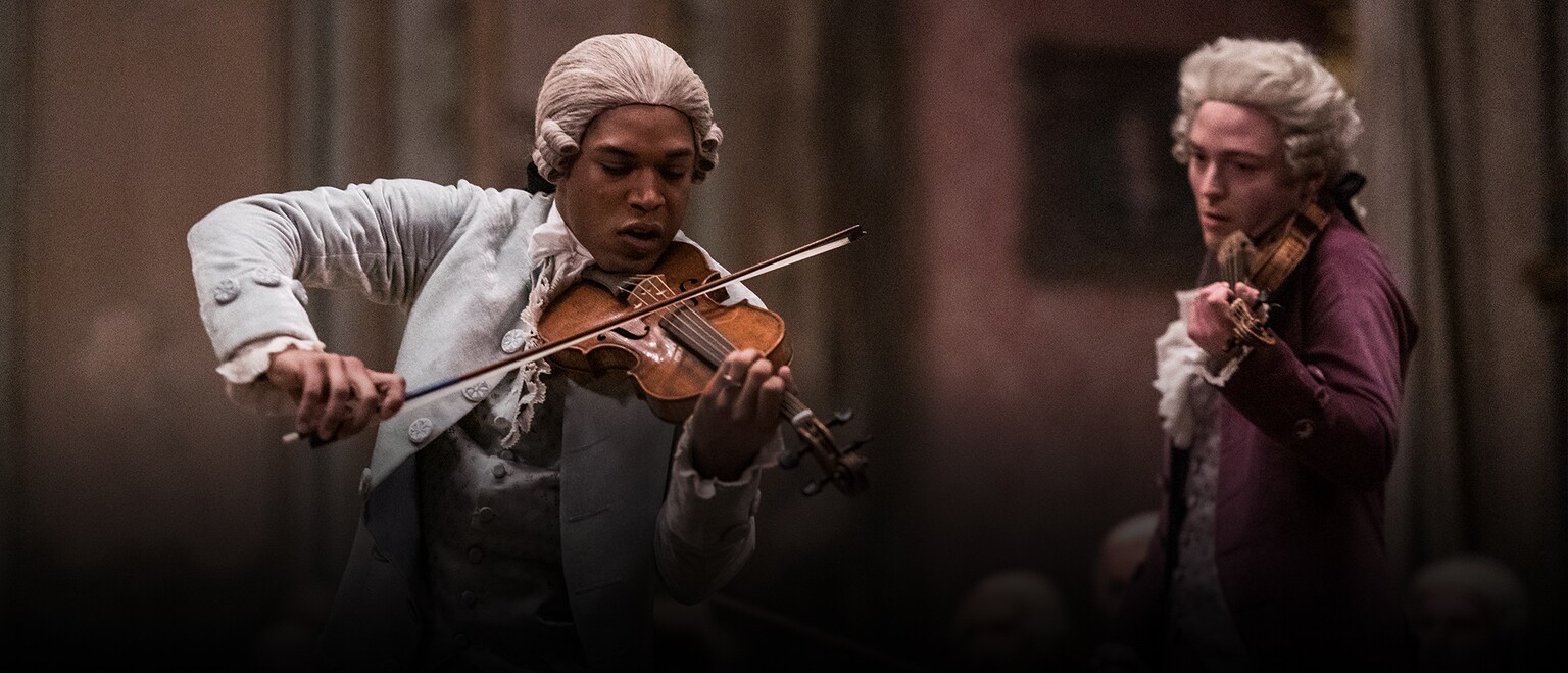 An image featuring Kelvin Harrison Jr. as Chevalier de Saint-Georges, holding a violin and playing with it while wearing traditional white dress of the period, as another violinist looks on waiting to play.