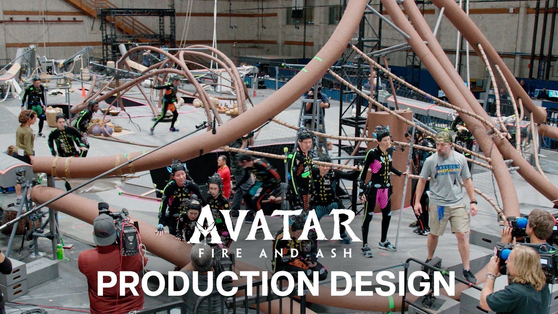 Image of a large sound stage with several actors in motion-capture suits along with several crew members standing below piping-like structures. | Avatar: Fire and Ash | Production Design