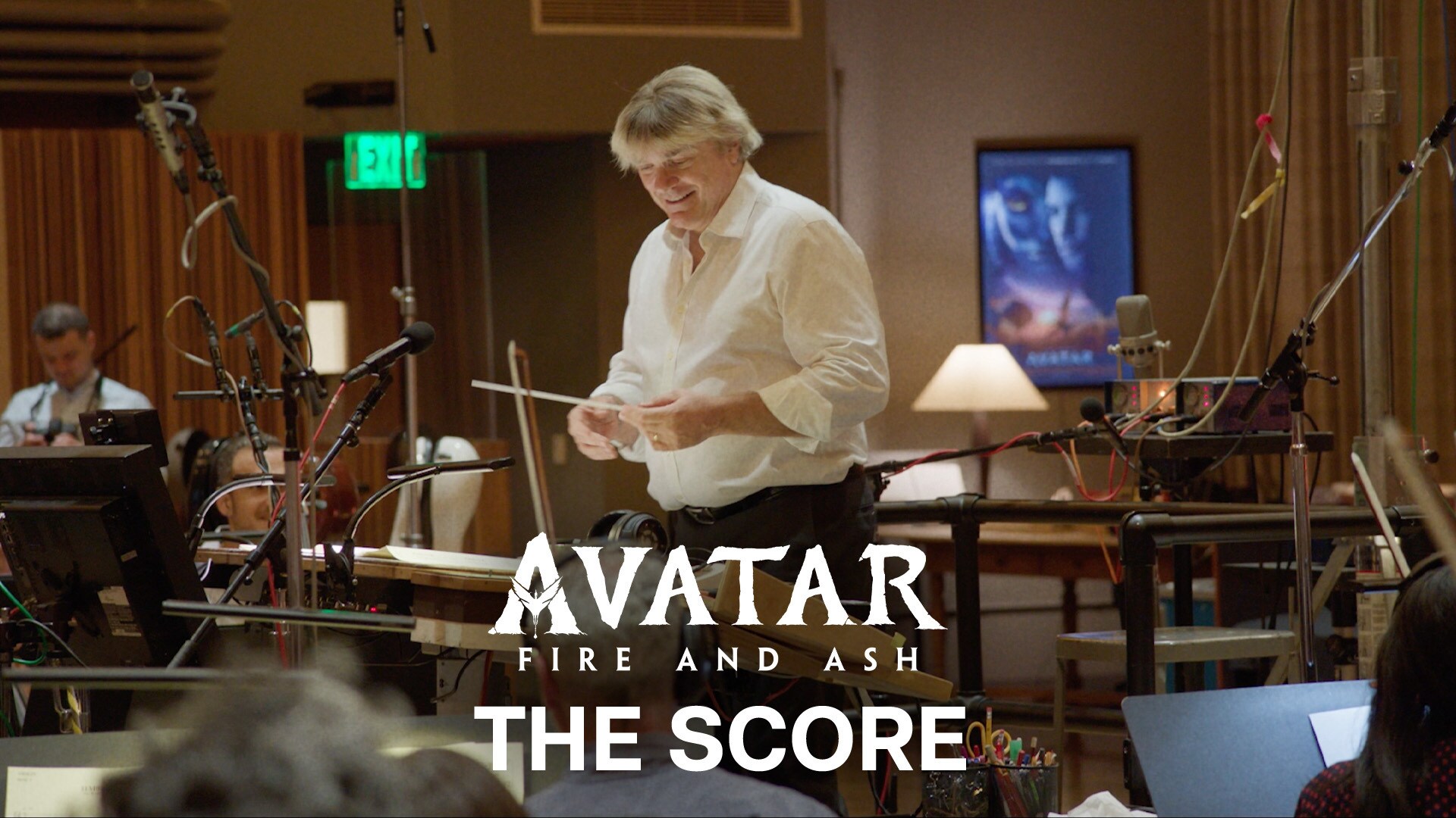 Image of composer Simon Franglen holding a baton while standing in a room in front of an orchestra. | Avatar: Fire and Ash | The Score