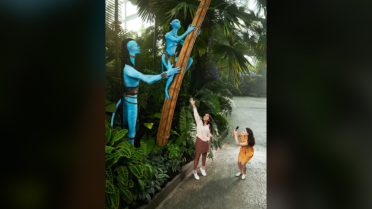 Visitors pose and take pictures with life-size Na'vi models climbing a tree.