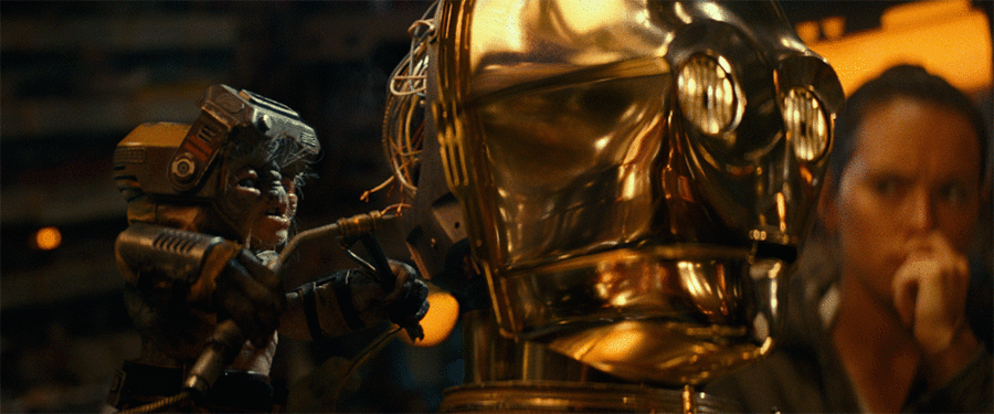 Babu Frik works on the electronics in C-3PO's head with Rey in the background, in a GIF.
