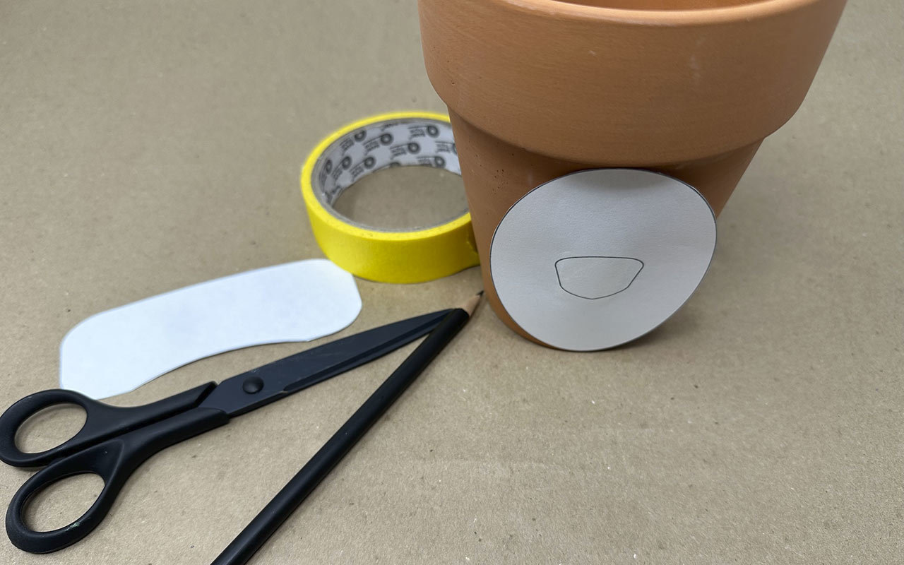 Use the masking tape to stick the oval shape to the 4” clay pot. Trace it with a pencil. Remove the stencil and stick it to your work surface.
