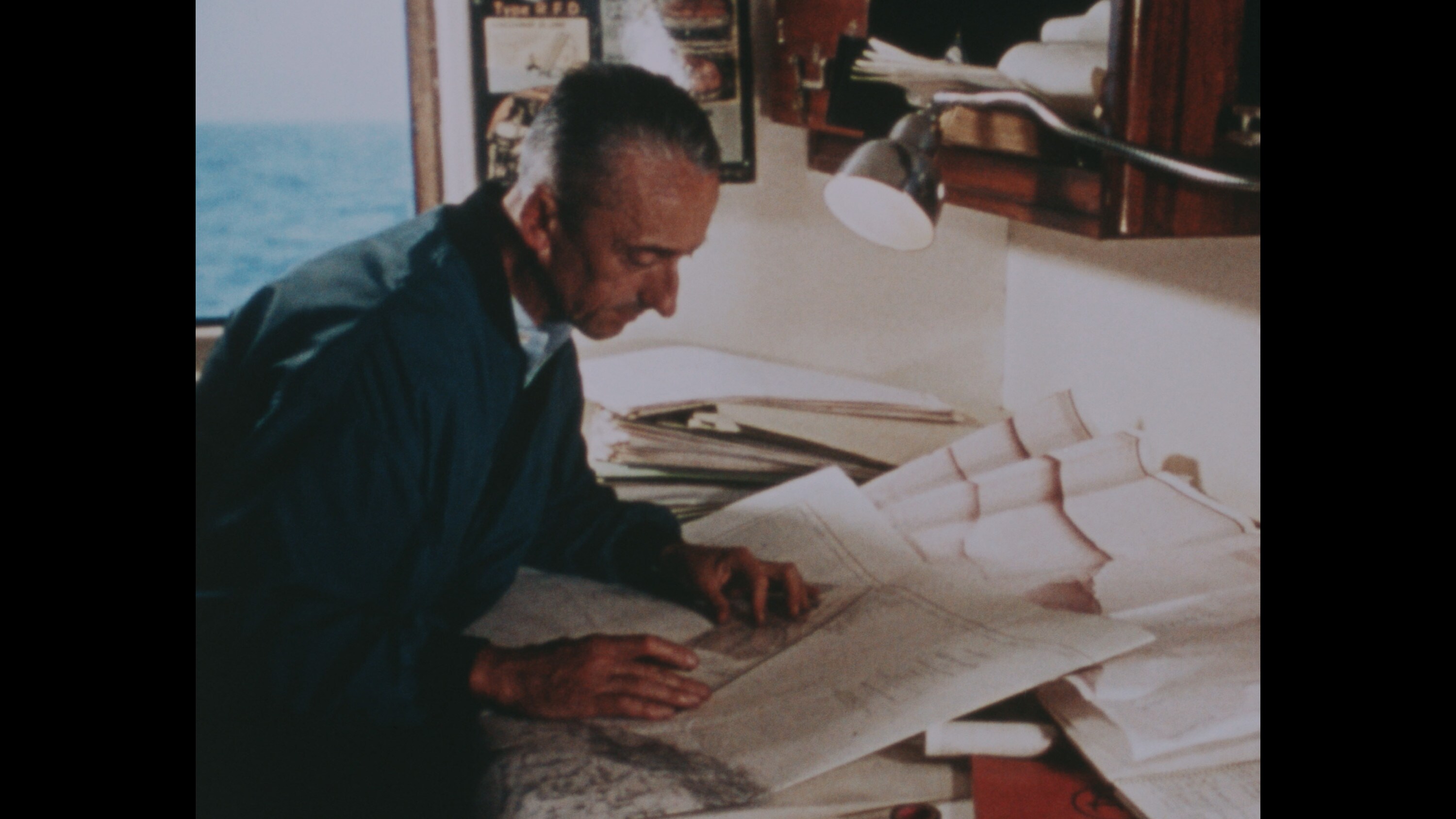 Jacques Cousteau examines charts aboard his ship, Calypso. (Credit: The Cousteau Society)