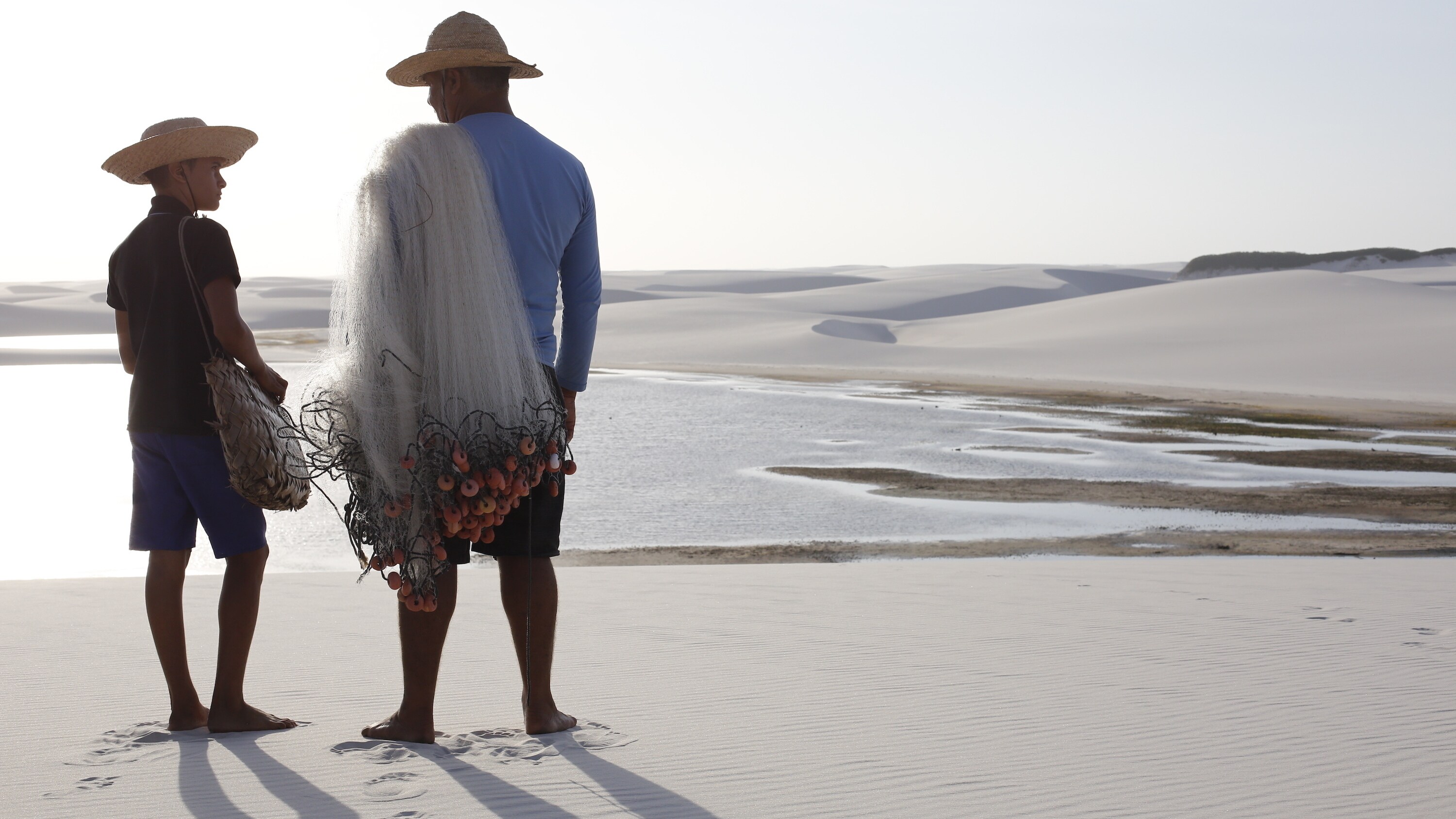 Fisherman Zeca Lira and his grandson  Jonhis look for signs of fish in a shallow pool amid the dunes of Lençóis Maranhenses.  (National Geographic for Disney+/Davinia Goodhart)