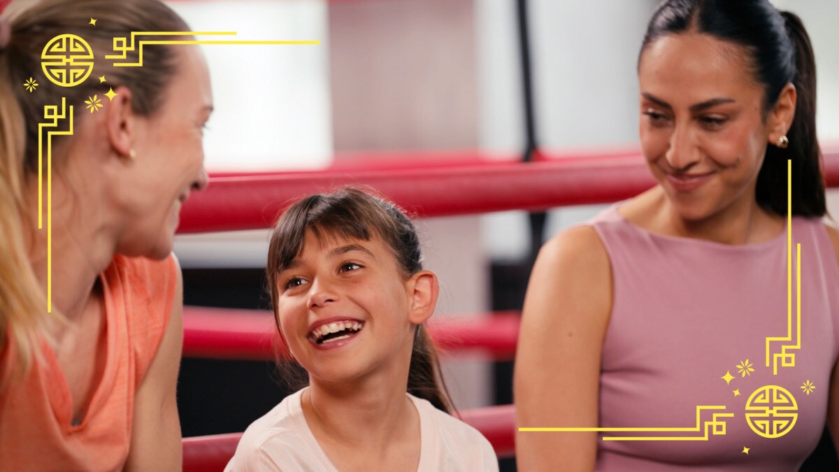 Melissa Khalaj, Christine Theiss und Gewinnerkind Sofia sitzen vor einem Boxring und freuen sich