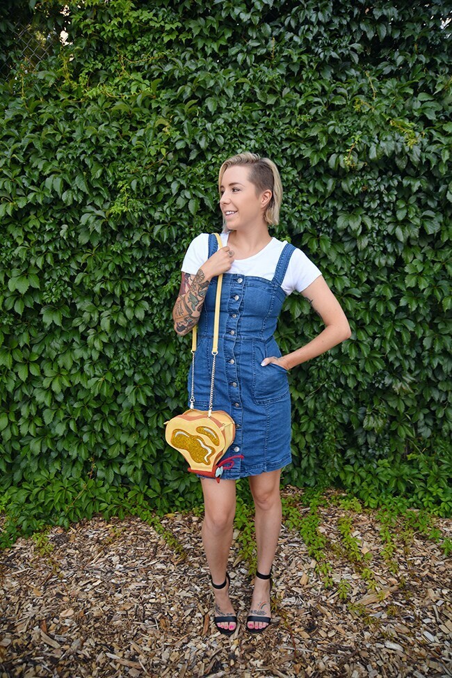 woman's purse that looks like a butterfly composed of pieces of toast with butter on it. The woman is wearing a denim overall dress