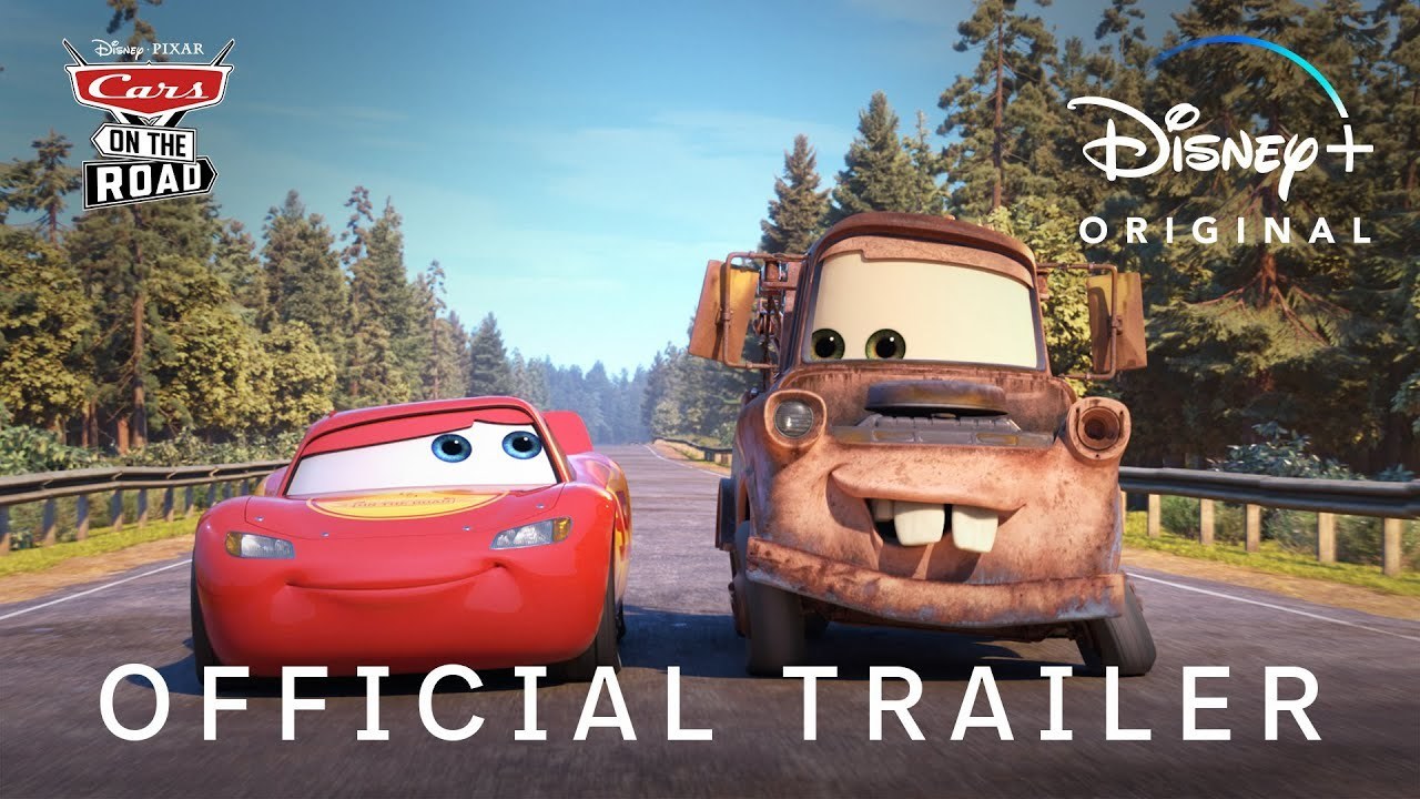 Lightning McQueen and Mater look at each other on a bright and sunny road, lined with trees on both sides.