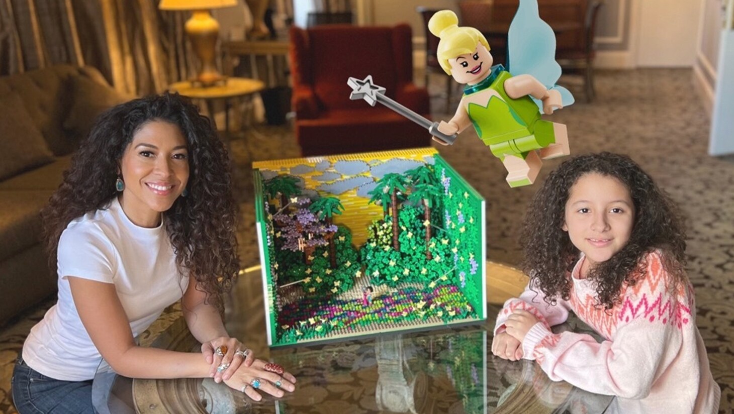 Image of a LEGO diorama on a table between a woman and a young girl. An image of a LEGO Tinkerbell is superimposed on the image.