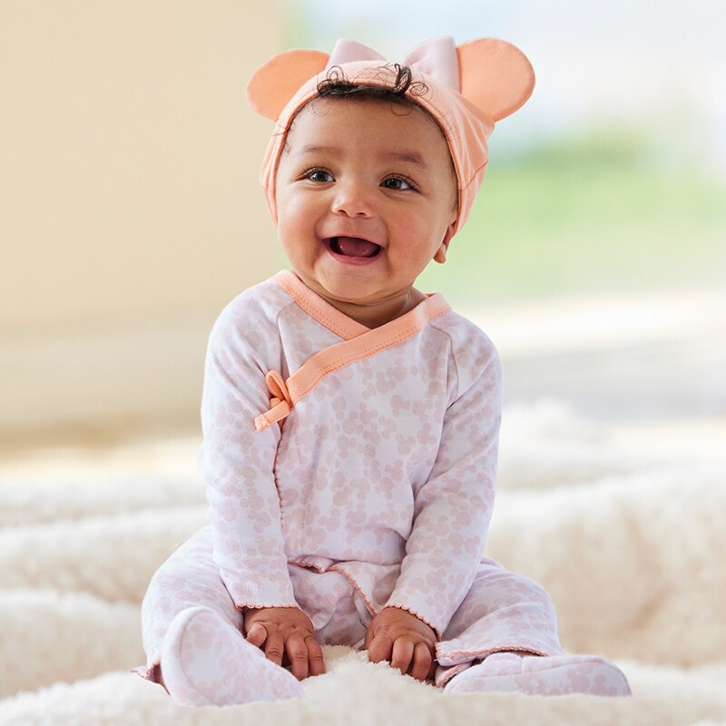 A smiling baby sits on a blanket wearing shopDisney baby clothing.