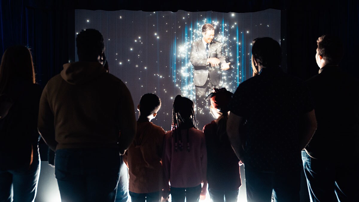 Gäste stehen im Dunkeln vor einer Leinwand, auf der Walt Disney zu sehen ist.