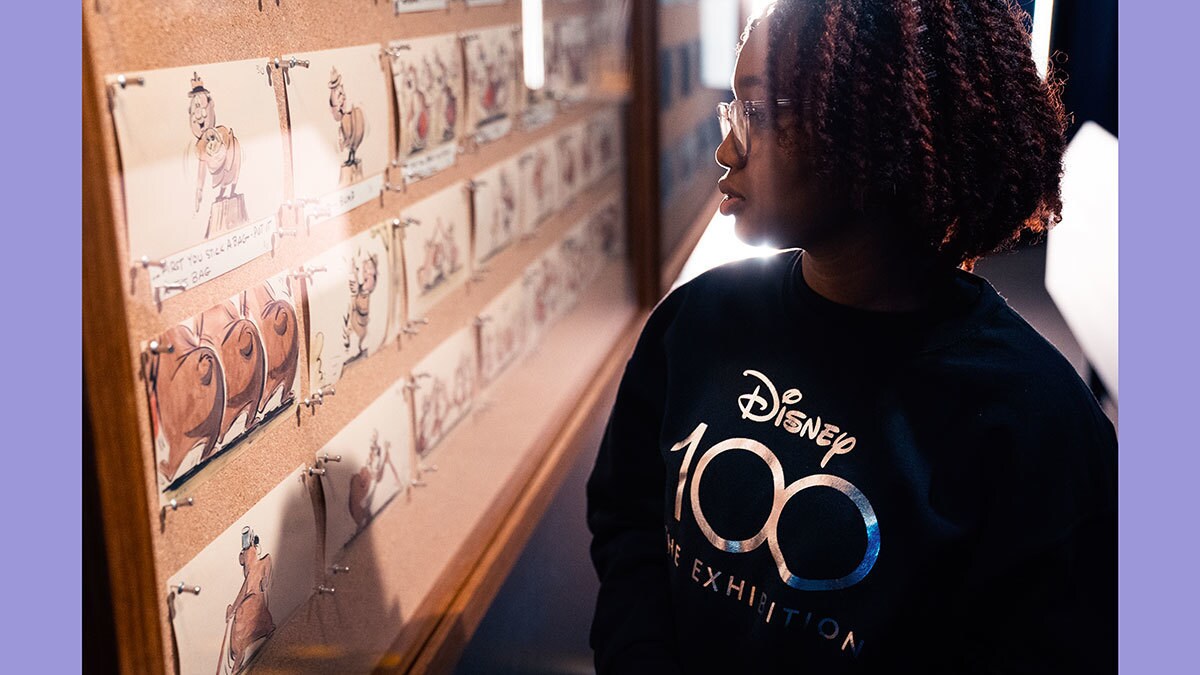 Eine Frau schaut in eine aufgehängte Vitrine mit Skizzen von Disney Filmcharakteren.