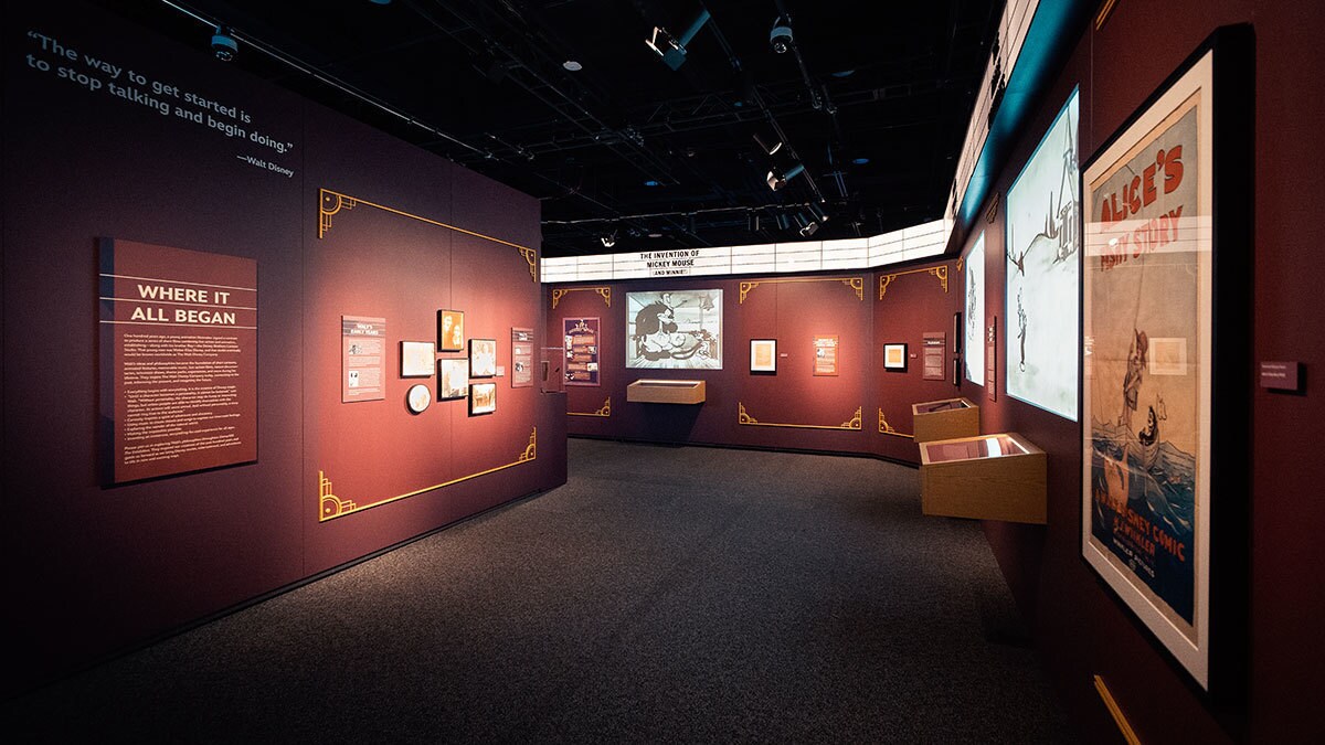 Dunkel gefärbte Ausstellungswände zeigen verschiedene Bilder und Texte über die Anfänge von Disney.