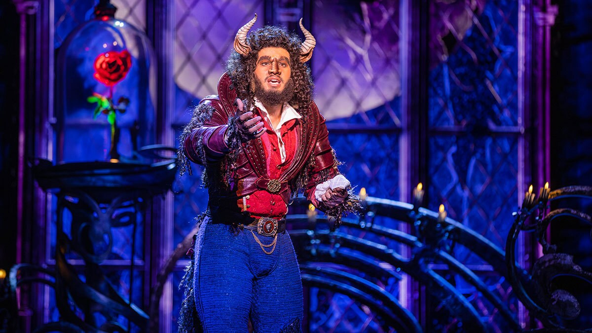 Das Biest streckt die Arme nach vorne. Sein Mund ist geöffnet. Im Hintergrund ist die Rose zu sehen.