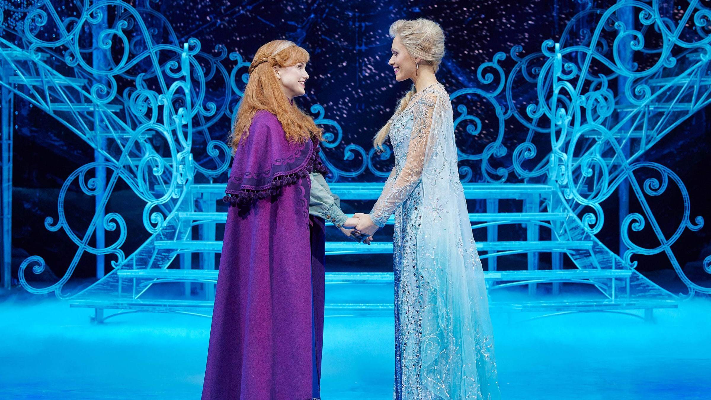 Elsa und Anna, wie sie sich im Eispalast händehaltend gegenüberstehen und gegenseitig anlächeln.