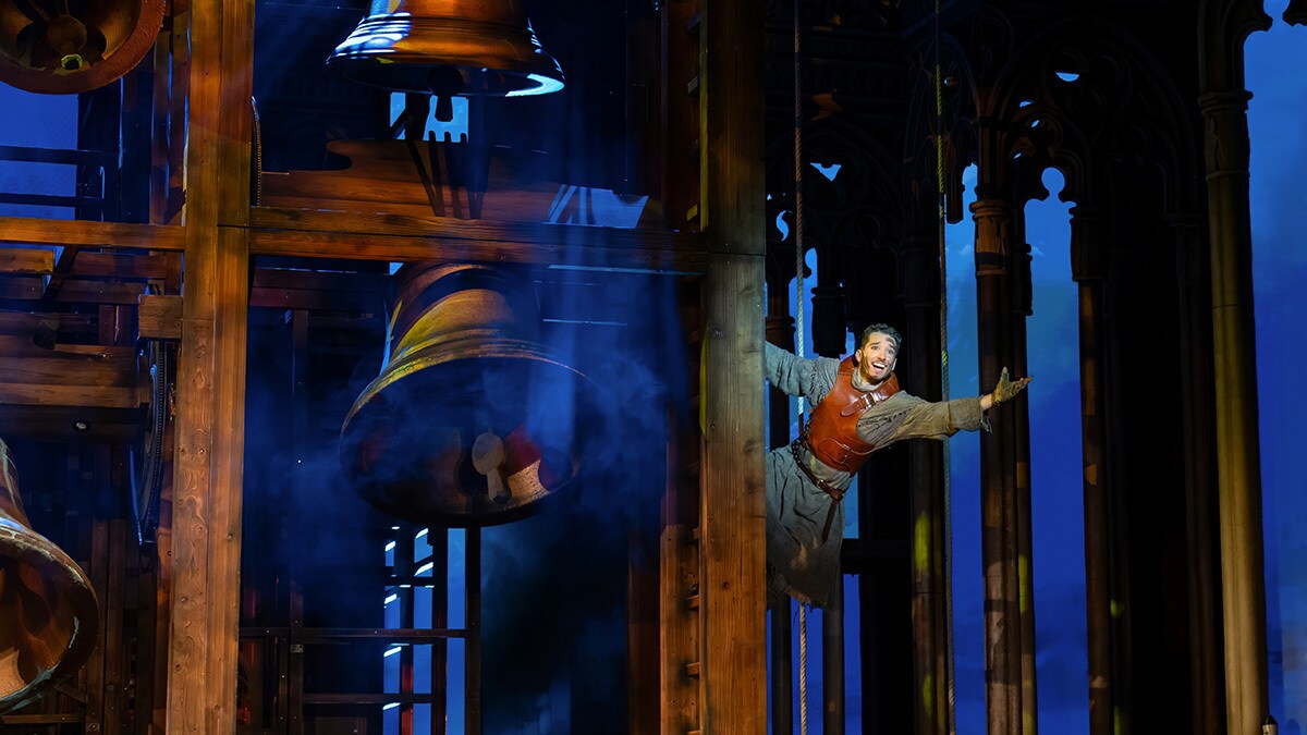 Quasimodo hängt rechts von der Kirchenglocke und streckt freudig seinen Arm aus.